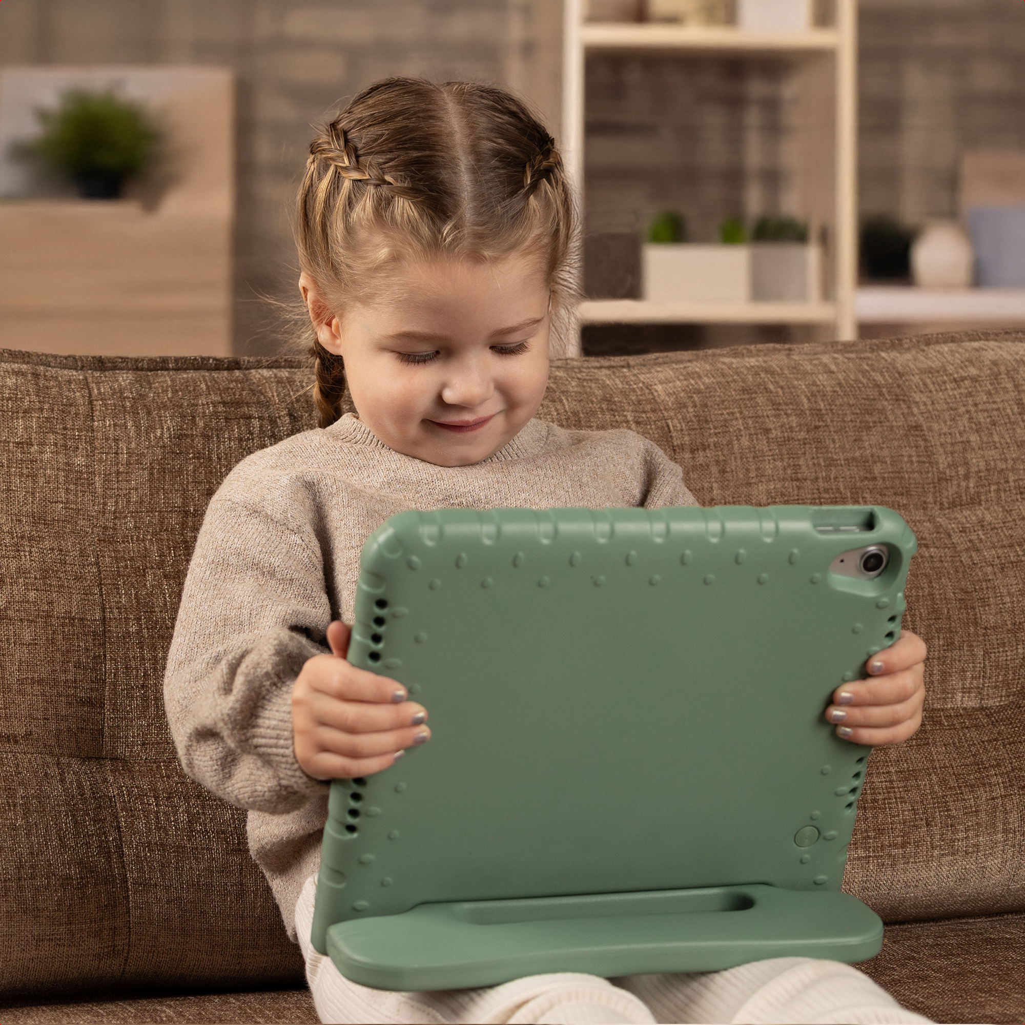 Een meisje met vlechten kijkt naar een tablet. Ze zit op een bruine bank en houdt een groene tablethoes vast.