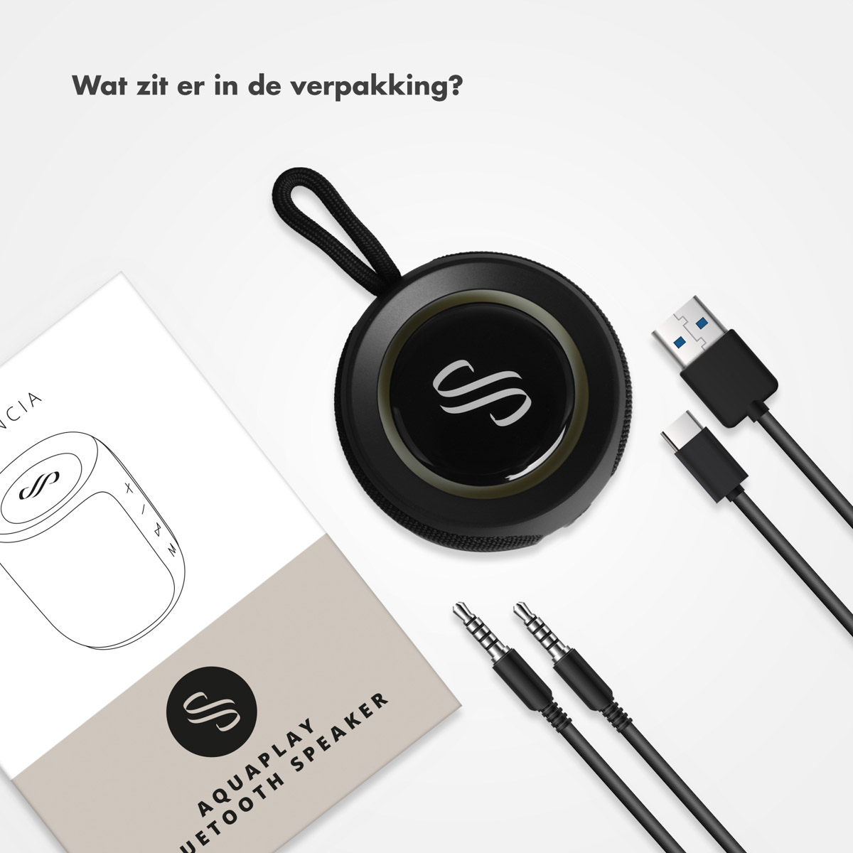 Zwarte speaker, kabels en handleiding op wit oppervlak. De speaker heeft een logo. Kabels zijn USB en audio jacks.