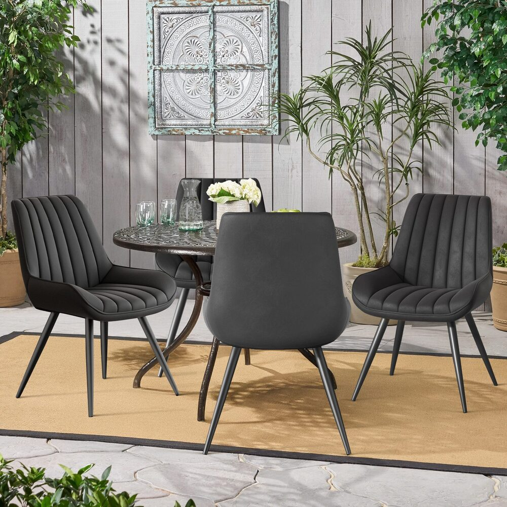 Szene im Freien mit rundem Tisch und vier schwarzen Stühlen. Pflanzen und dekorative Wandkunst umgeben den Sitzbereich.
