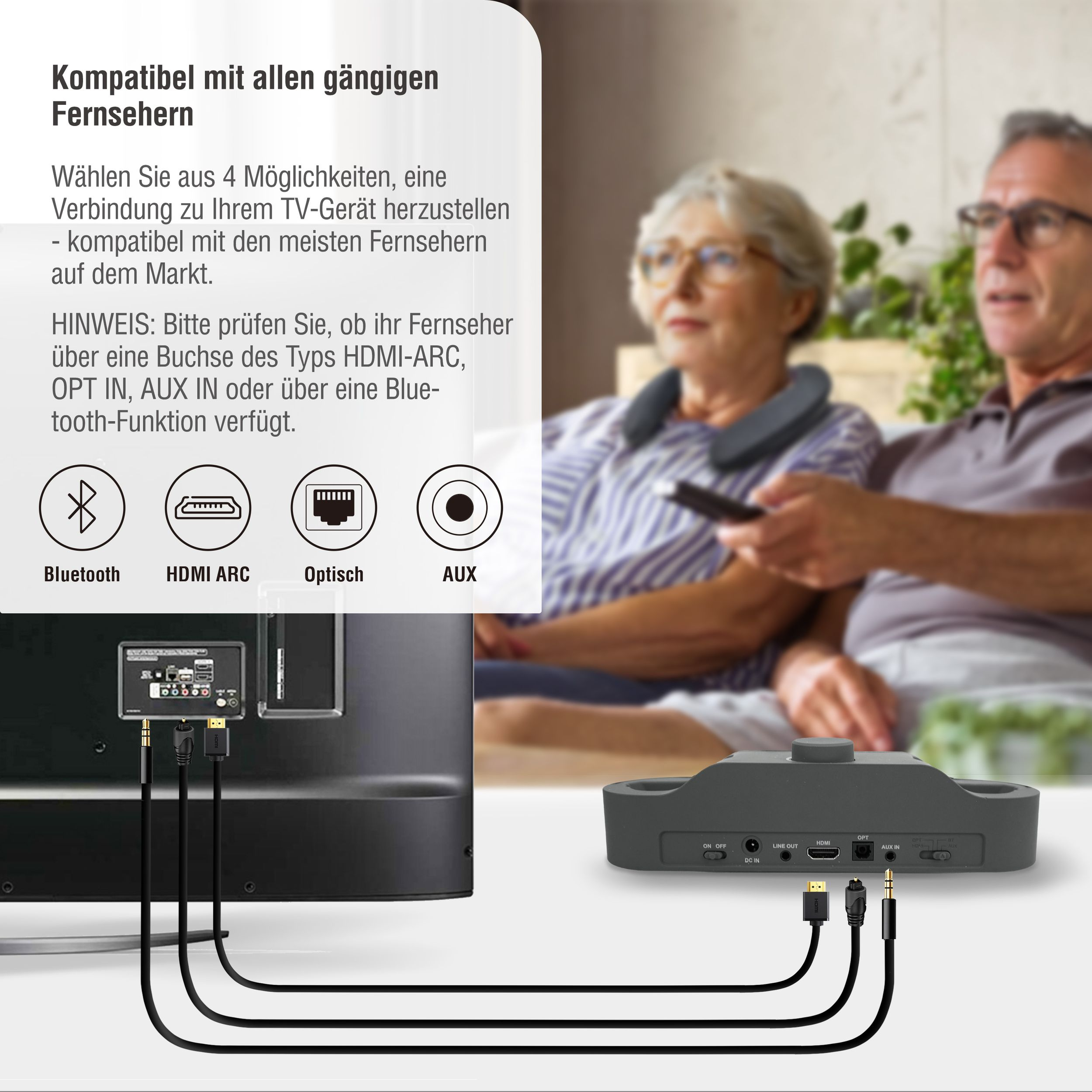 Das Bild zeigt ein Fernsehgerät mit angeschlossenen Kabeln an ein Gerät. Zwei Personen sind im Hintergrund unscharf.