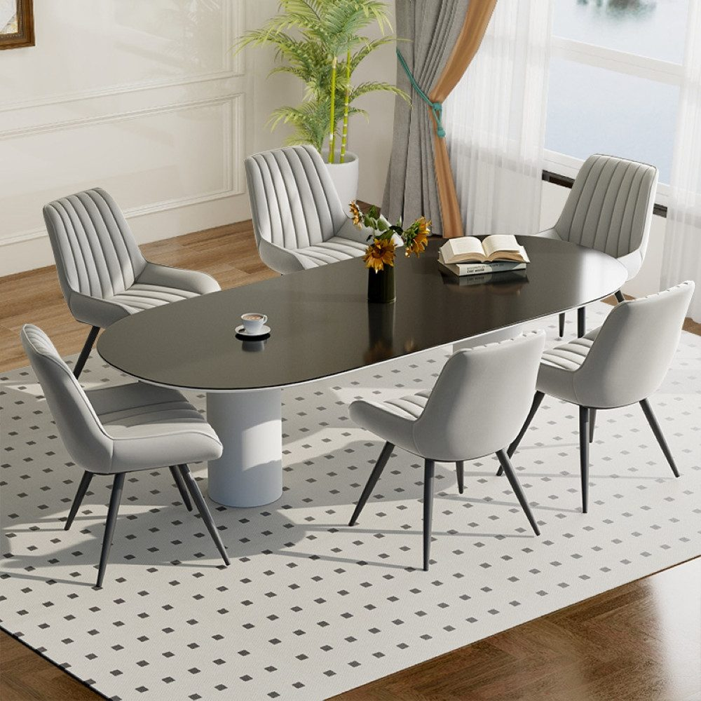 Ein Esszimmer mit Tisch und sechs Stühlen. Eine Tasse Kaffee und Blumen stehen auf dem Tisch. Ein Fenster mit Vorhängen ist sichtbar.