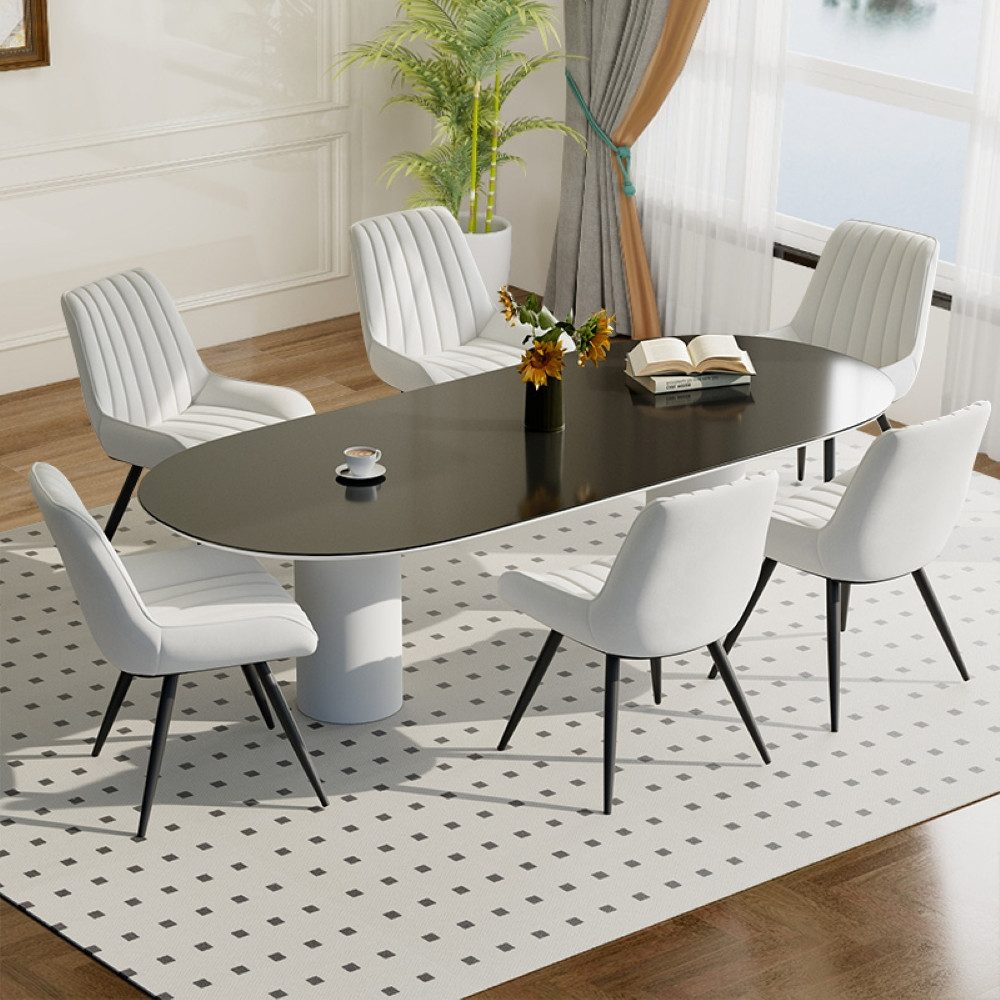 Ein Esszimmer mit ovalem schwarzem Tisch, weißen Stühlen, einem Teppich und einer Pflanze. Eine Kaffeetasse und Blumen auf dem Tisch.