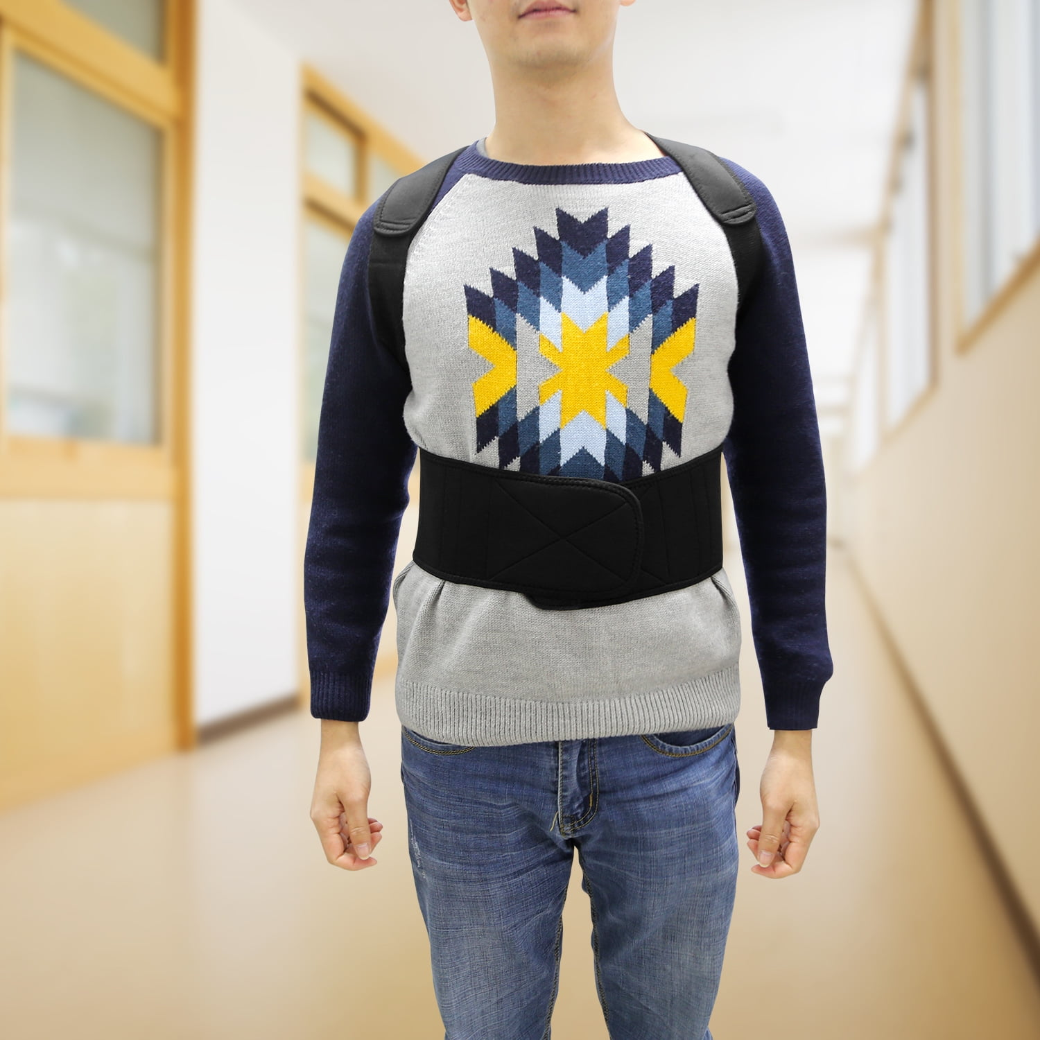 Ein Mann mit einer Haltungskorrektur über einem Pullover und Jeans steht in einem Flur. Der Hintergrund ist unscharf.