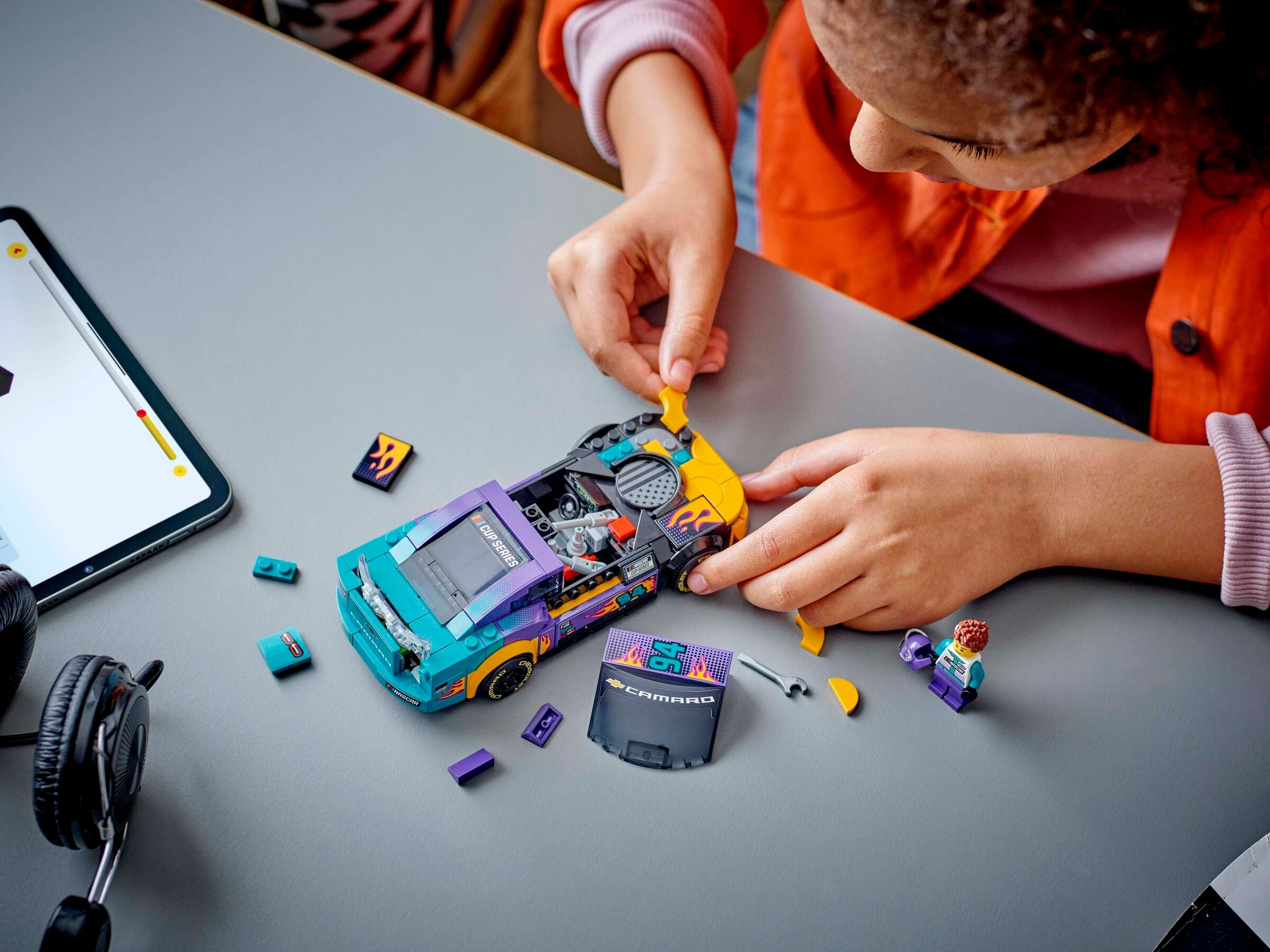 Ein Kind baut ein buntes Rennwagenmodell mit LEGO-Steinen auf einer grauen Oberfläche.