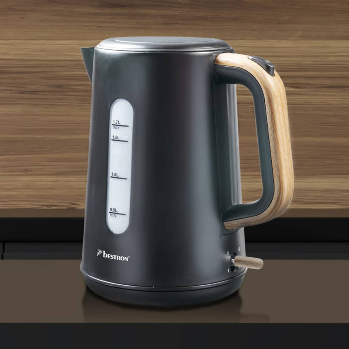 Un bollitore elettrico nero con manico in legno è su una superficie marrone. Ha un indicatore del livello dell'acqua e un interruttore in legno.