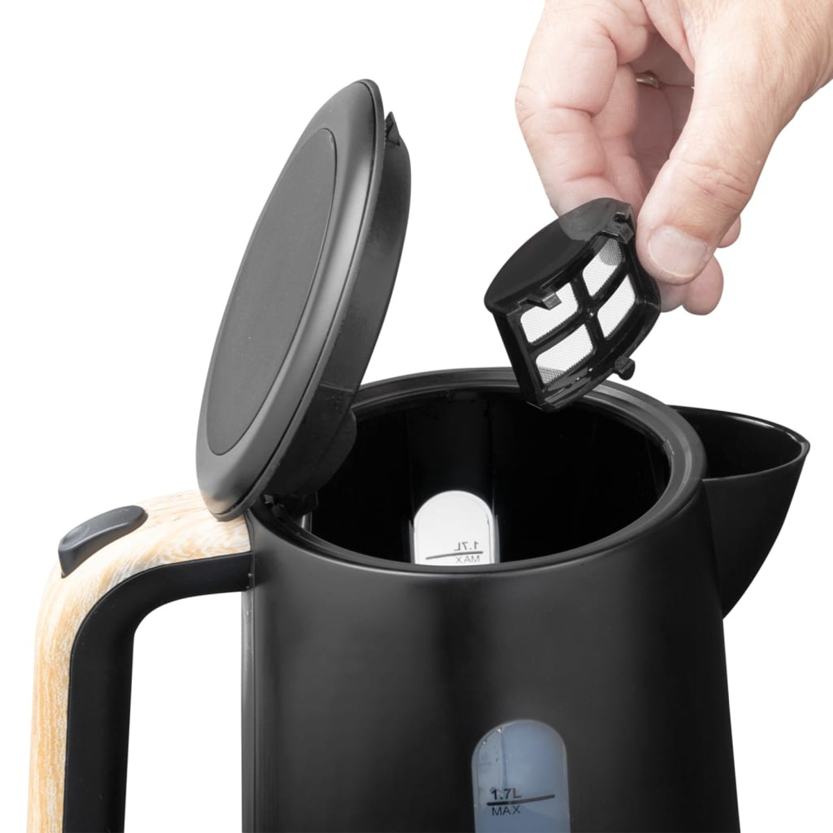 Una mano tiene in mano un infusore da tè nero sopra un bollitore elettrico nero aperto. Il coperchio è aperto. Il bollitore ha un manico in legno.