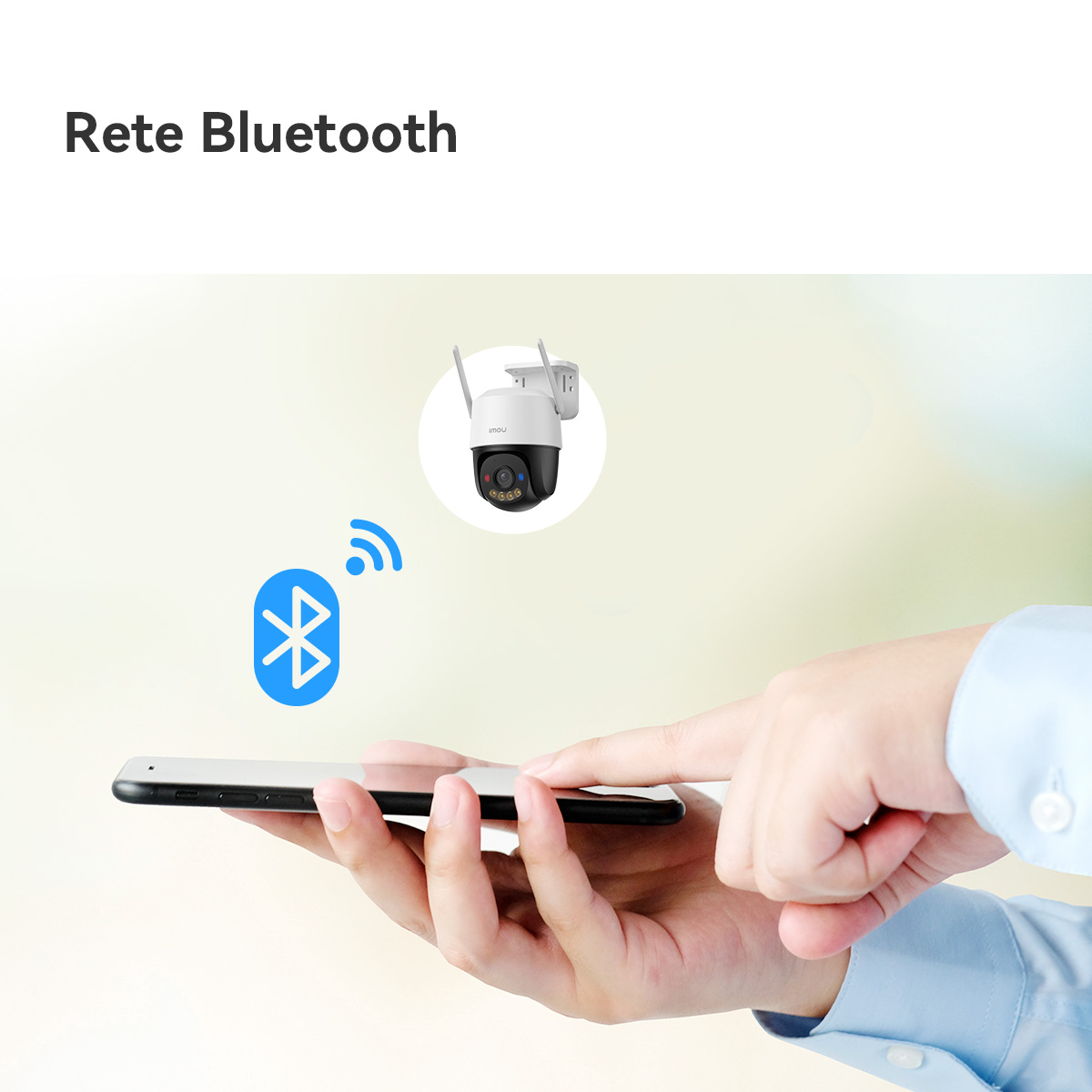 Ręka trzyma telefon, połączony przez Bluetooth z kamerą bezpieczeństwa. Kamera jest biało-czarna, z antenami.