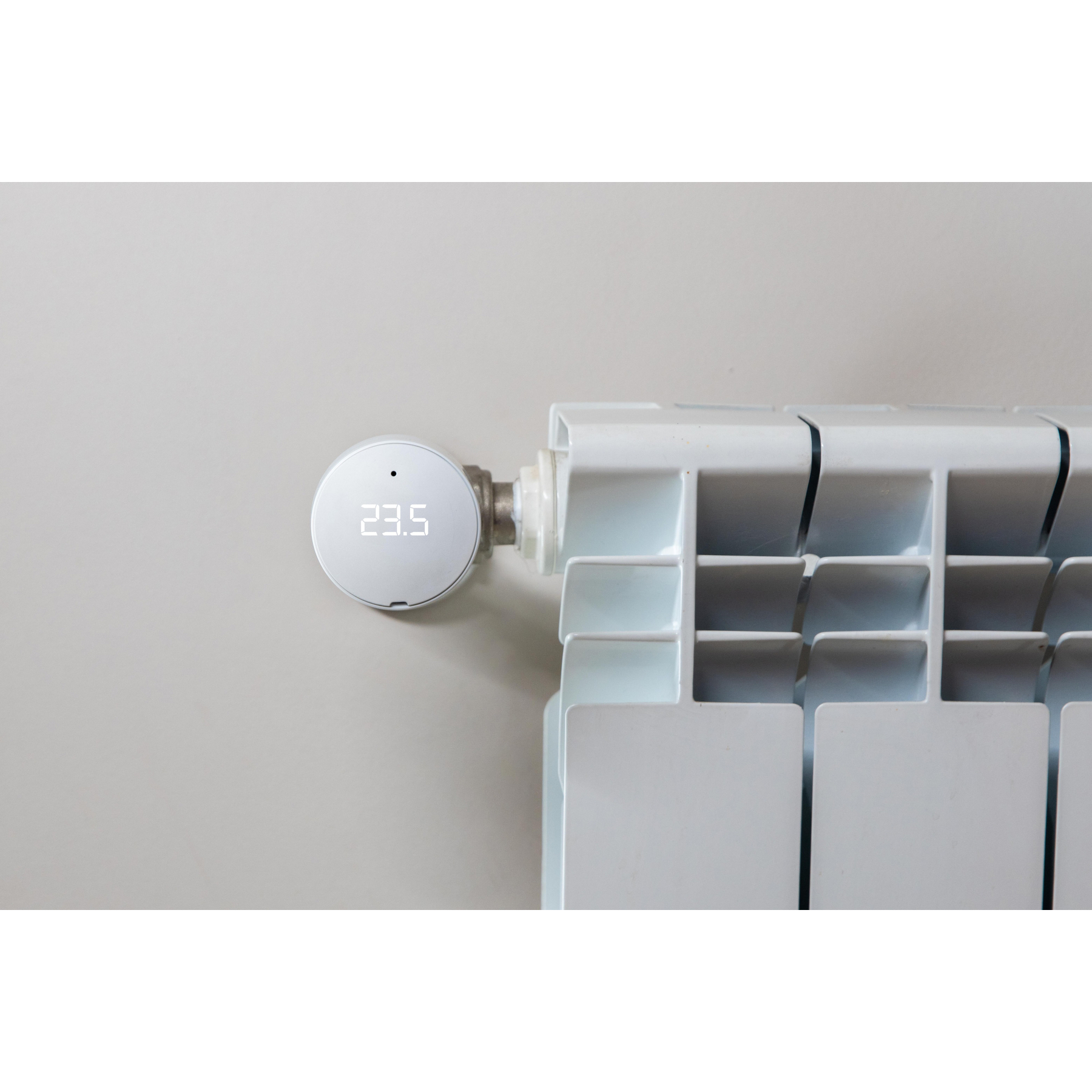 Biały grzejnik z cyfrowym termostatem pokazującym 23,5 stopnia przymocowany do ściany. Ściana jest szara.