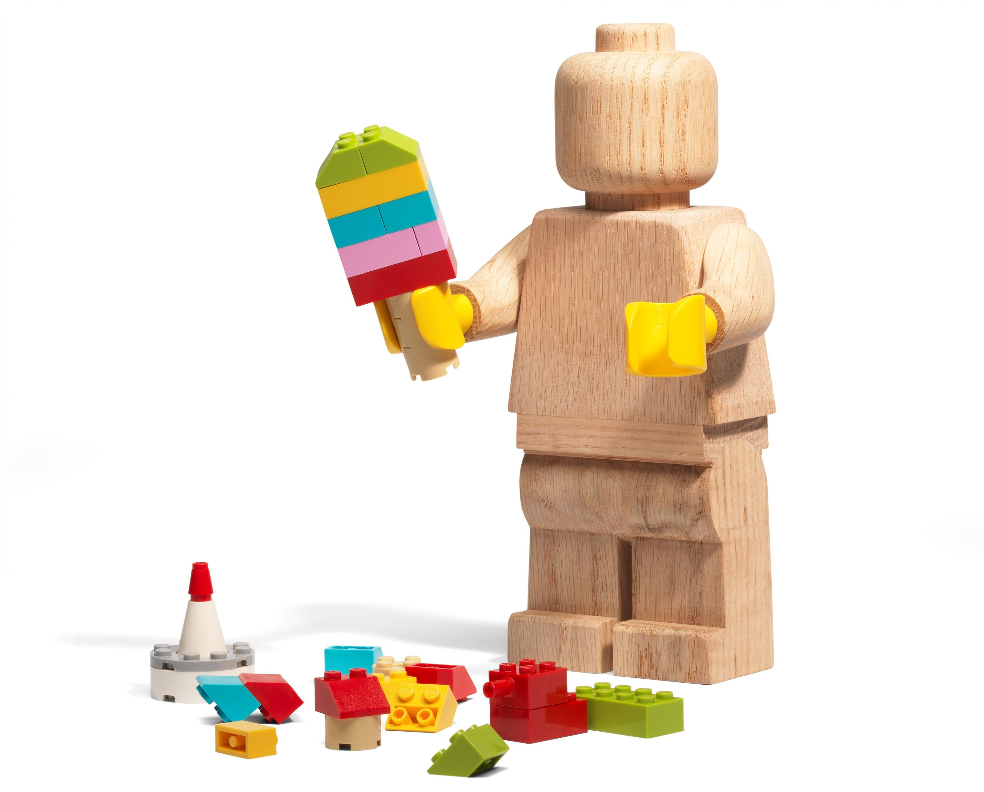 Figura di legno che tiene un ghiacciolo Lego. I mattoncini Lego sono sparsi sulla superficie bianca.
