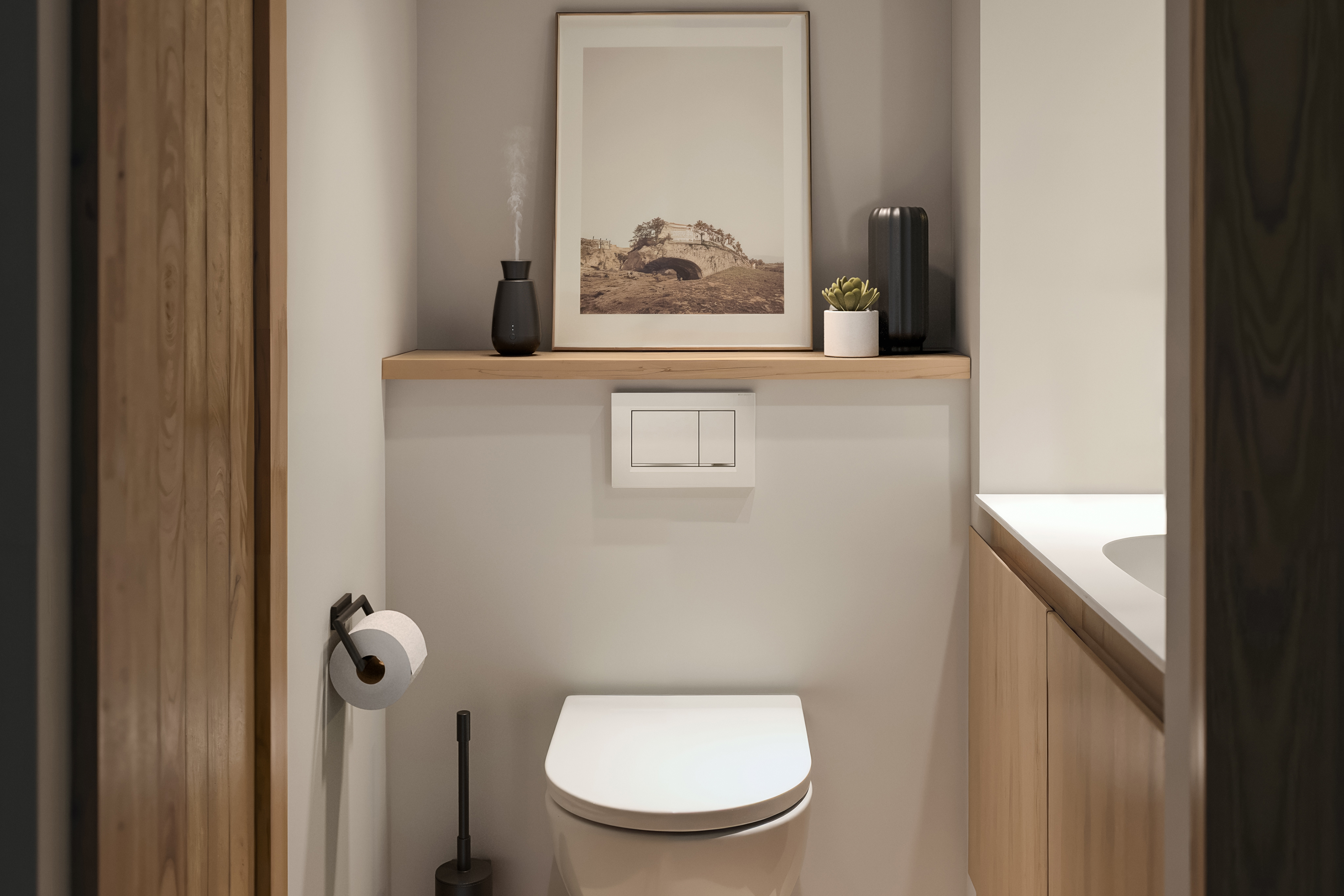 A modern bathroom with a toilet, shelf with decor, and a wooden door on the side.