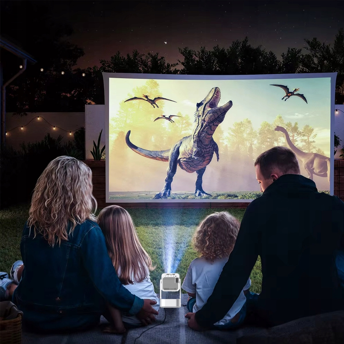 Rodzina ogląda film o dinozaurach na ekranie na zewnątrz w nocy. Przed nimi stoi projektor.