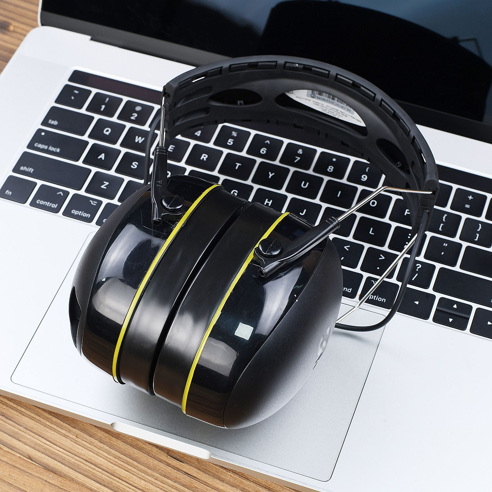 Cuffie nere con dettagli gialli su tastiera di laptop. Il laptop è su superficie di legno.