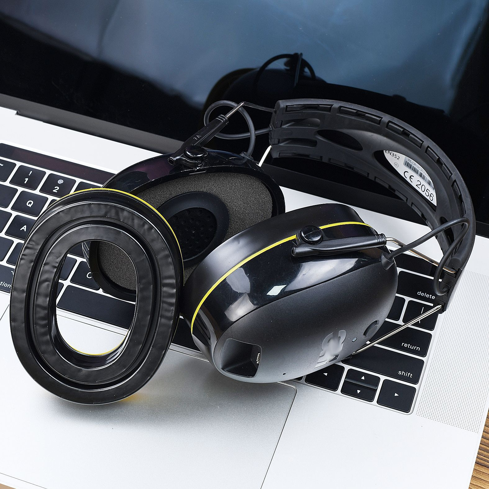Cuffie nere con dettagli gialli su tastiera laptop. Sfondo: schermo del laptop.
