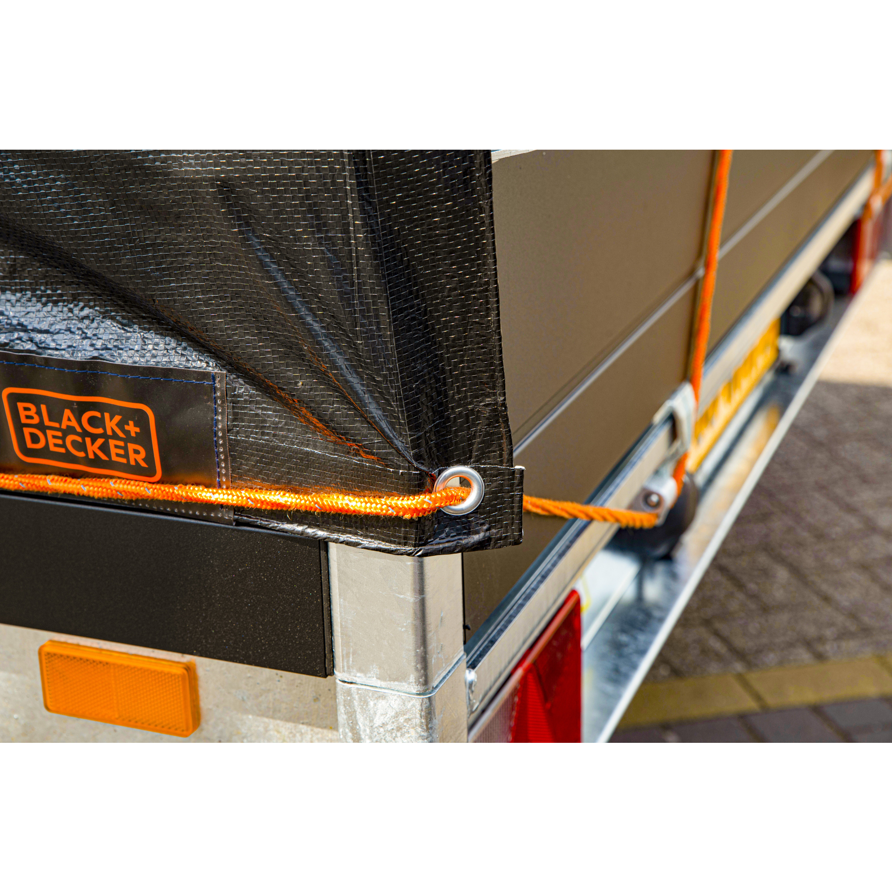 Un primo piano di un rimorchio con una copertura nera e una corda arancione. Il logo Black+Decker è visibile.