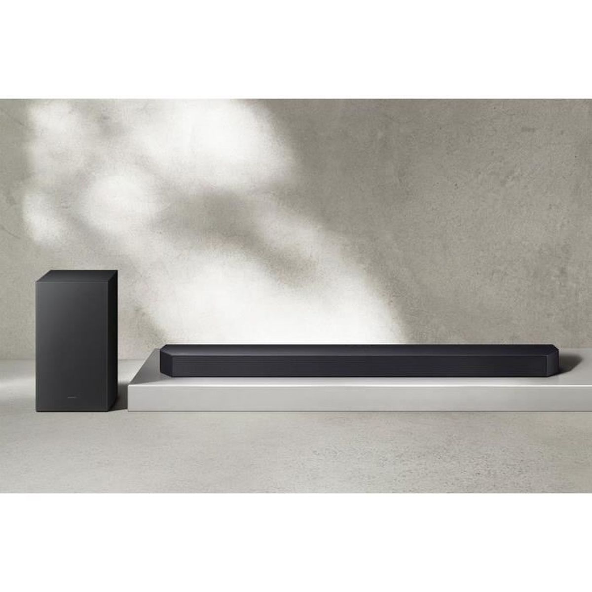 Eine schwarze Soundbar und ein Subwoofer auf einer weißen Plattform. Der Hintergrund ist eine strukturierte graue Wand.
