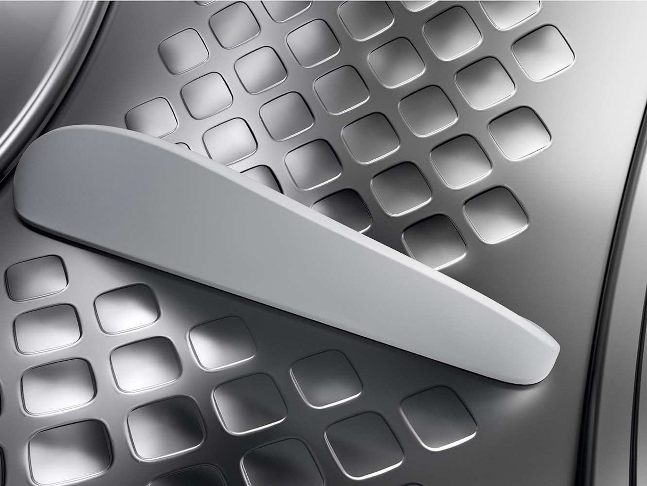 Zbliżenie metalowej powierzchni z białym uchwytem. Powierzchnia ma wzór kwadratowych wgłębień. Uchwyt jest lekko zakrzywiony.