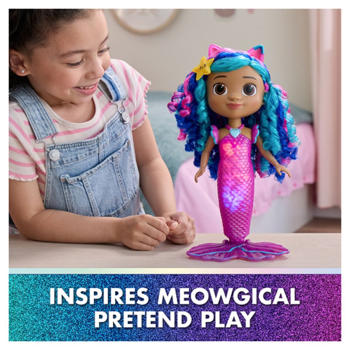 Ein Mädchen lächelt eine Meerjungfrauenpuppe mit blauem und pinkfarbenem Haar an. Die Puppe hat einen pinkfarbenen Schwanz und ein sternförmiges Accessoire.