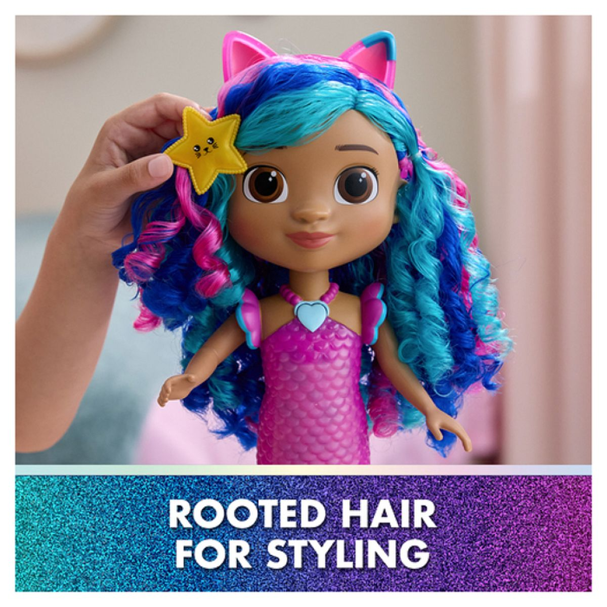 Eine Puppe mit blauem und pinkfarbenem Haar, Katzenohren und einem Stern-Haarclip wird von einer Hand gehalten. Sie trägt ein pinkes Kleid.