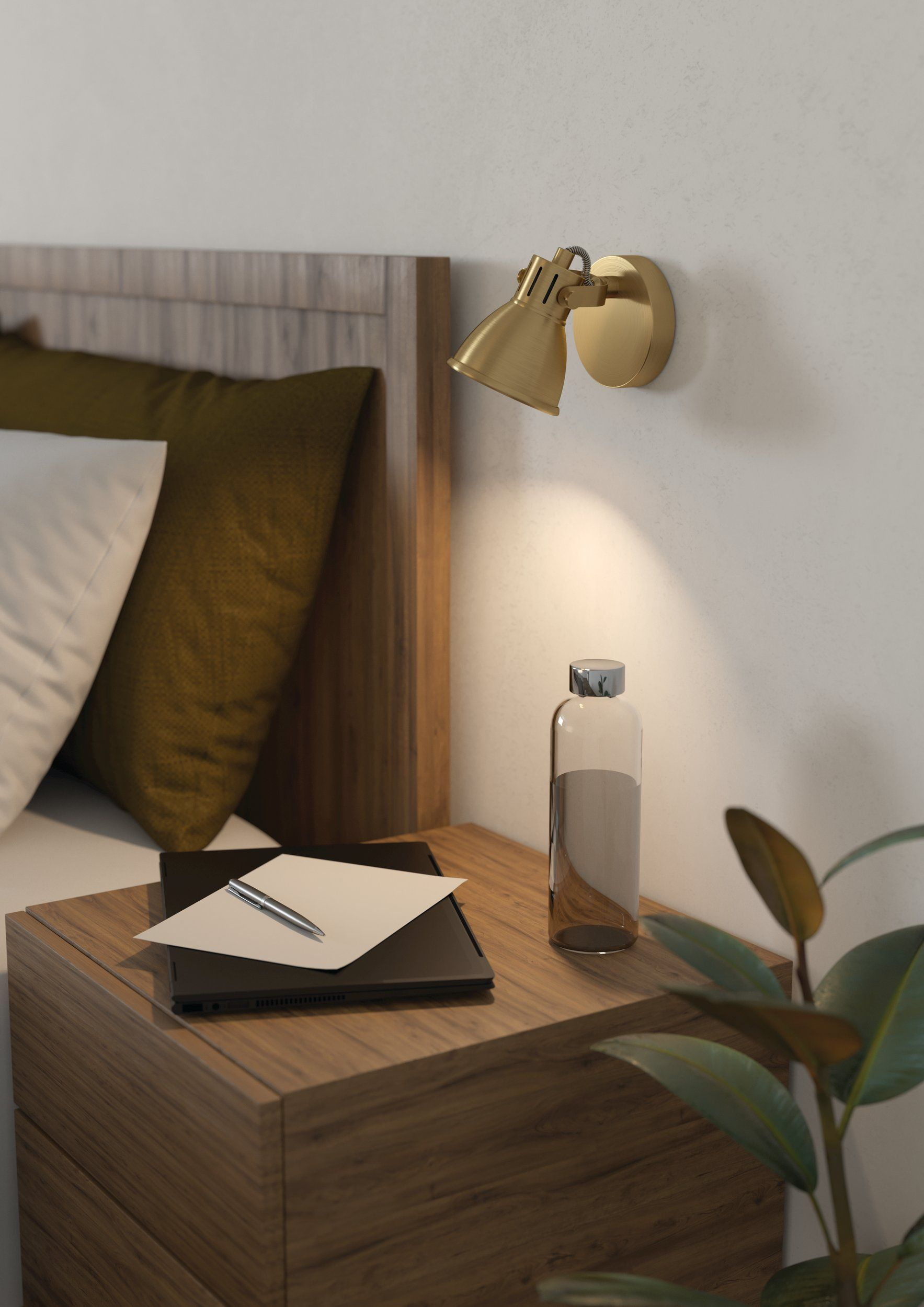 Nachttisch mit Lampe, Flasche und Laptop. Kissen im Hintergrund, eine Pflanze in der rechten Ecke.