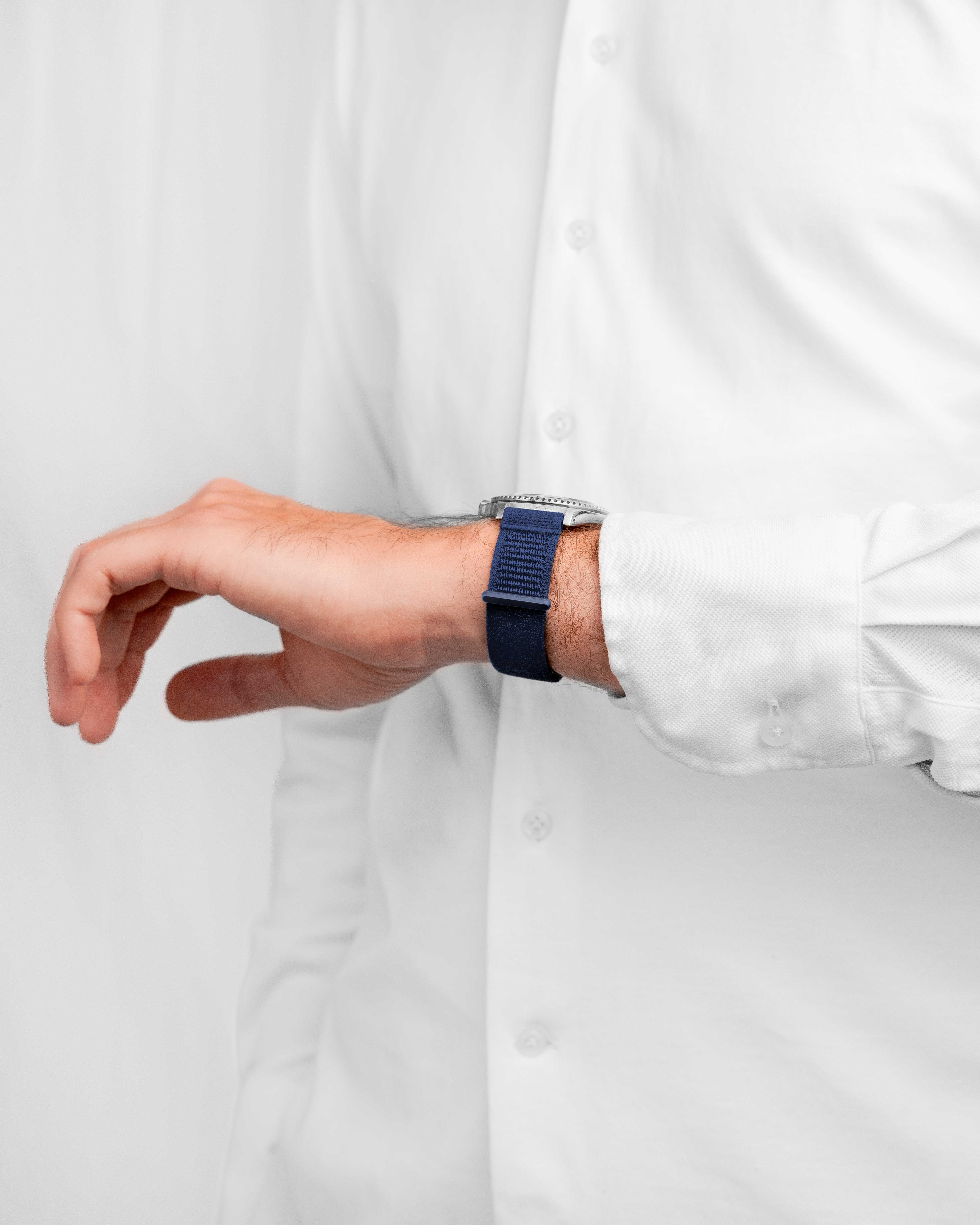Handgelenk eines Mannes mit blauem Armband und silberner Uhr. Er trägt ein weißes Hemd.