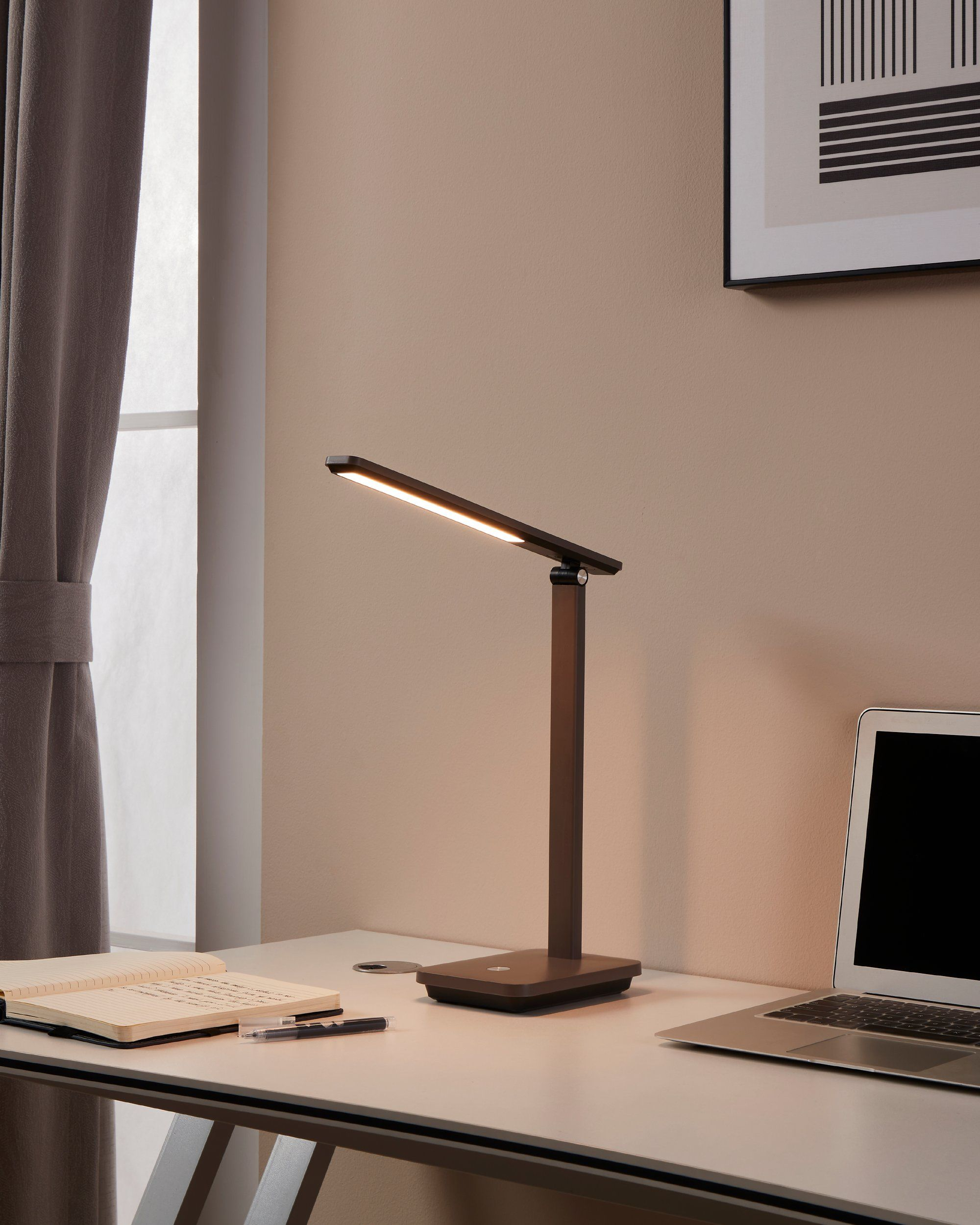 Eine Schreibtischlampe steht auf einem weißen Schreibtisch mit Laptop und Notizbuch. Licht kommt von der Lampe.
