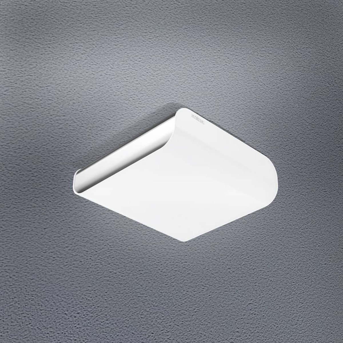 Un luminaire de plafond blanc carré avec des bords arrondis est monté sur un plafond gris texturé.