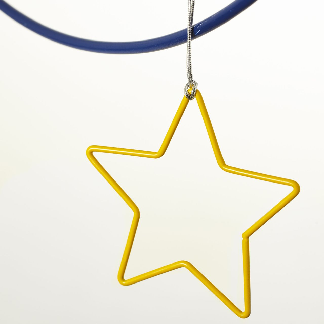 Ein gelber sternförmiger Schmuck hängt an einer silbernen Schnur unter einem blauen Reifen vor weißem Hintergrund.