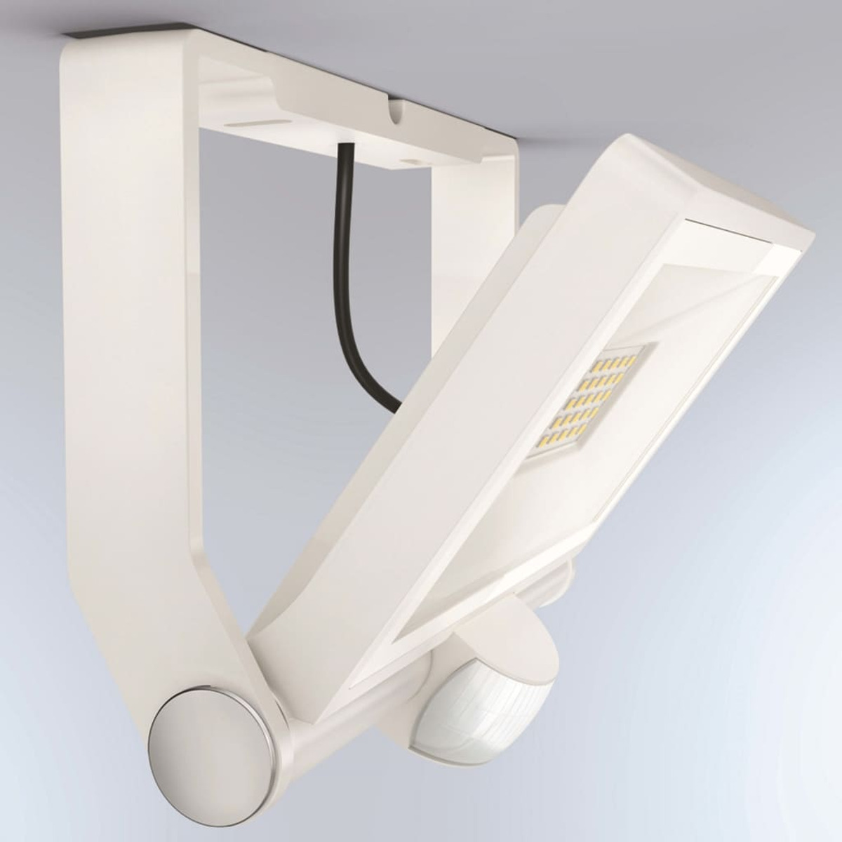 Weißer LED-Flutlichtstrahler an einer Halterung montiert. Schwarzes Kabel sichtbar. Bewegungssensor unten. Licht ist angewinkelt.