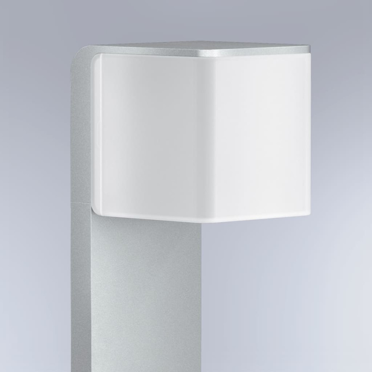Eine moderne, metallische Laterne mit quadratischer, weißer Leuchte. Der Pfosten ist silberfarben, vor einem grauen Hintergrund.
