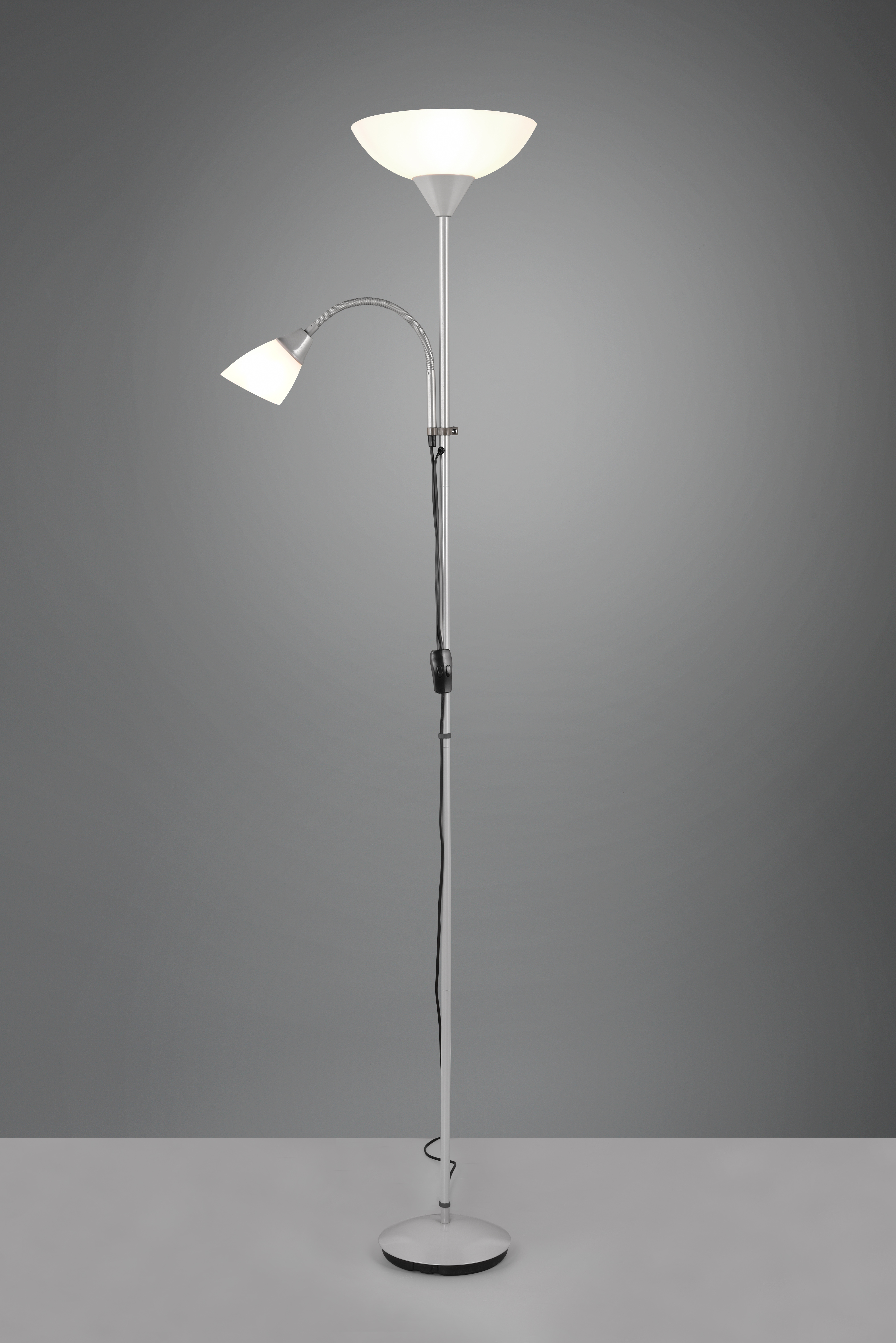 Una lámpara de pie moderna con dos luces, una en un brazo flexible. La base y el poste son plateados, las pantallas blancas.