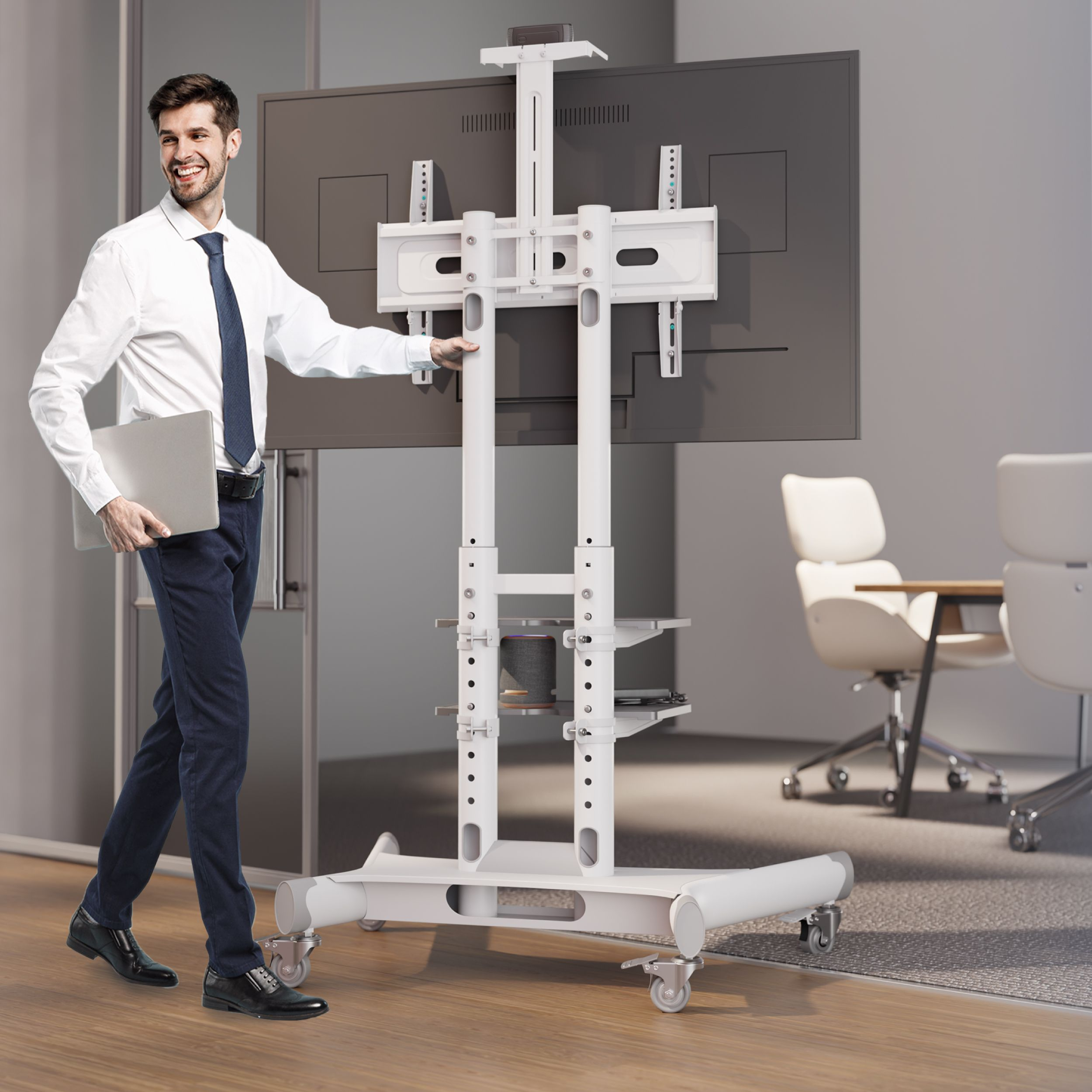 Mężczyzna trzyma laptopa, uśmiechając się. Przechodzi obok telewizora na mobilnym stojaku. W tle sala konferencyjna.