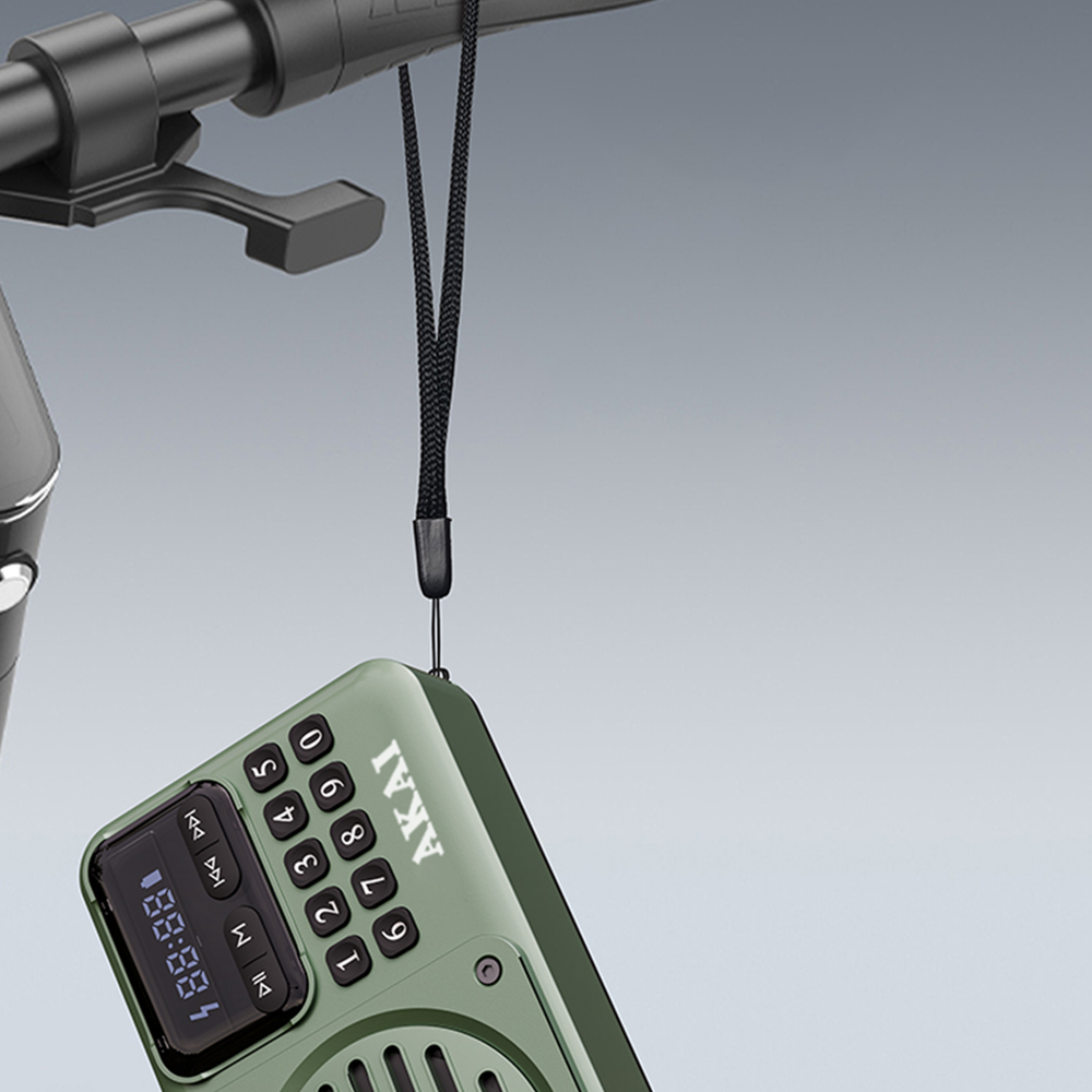 Oliwkowozielone radio AKAI zawieszone na czarnym pasku. Radio posiada ekran i klawiaturę.