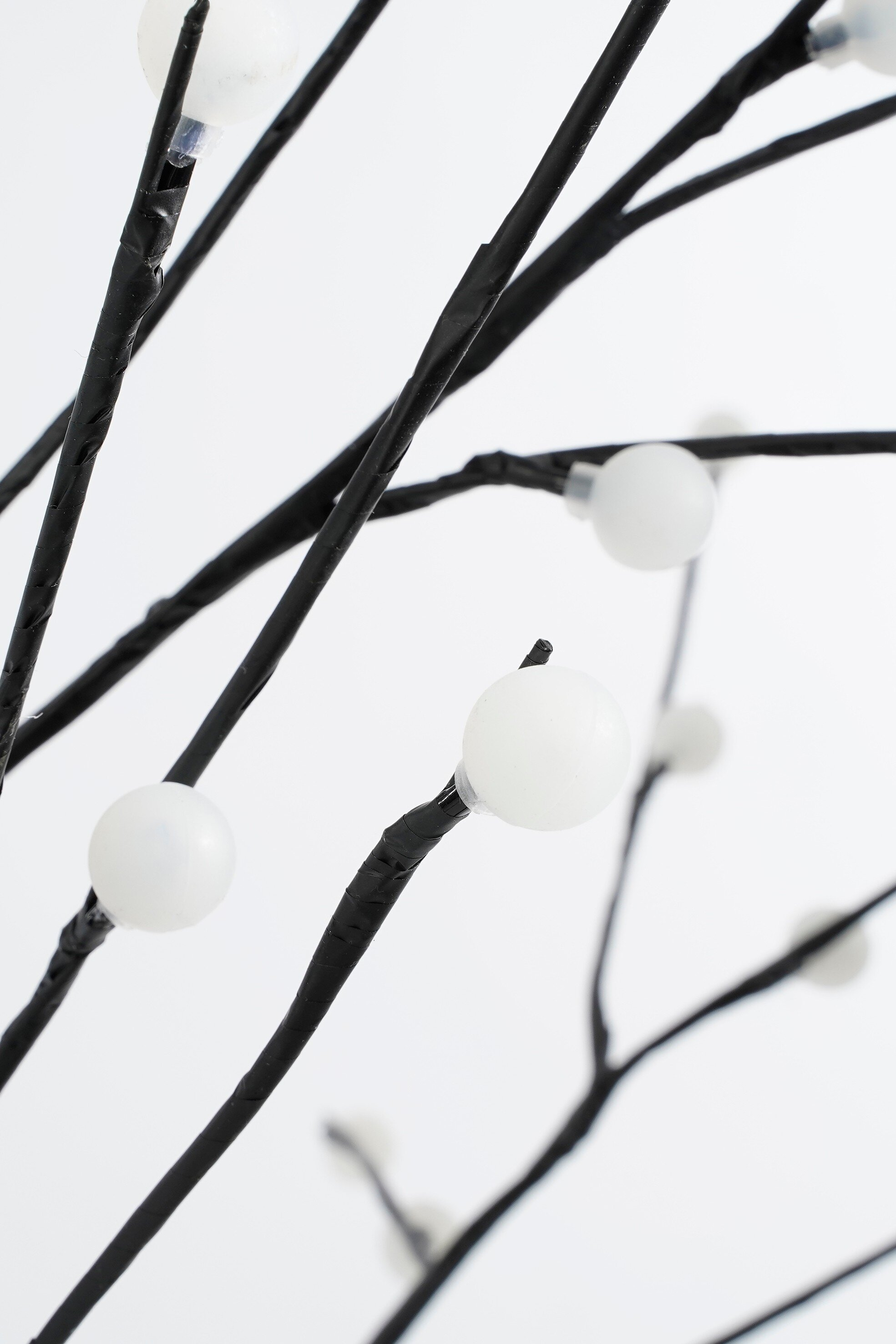 Gros plan d'un arbre décoratif avec des branches noires et de petites lumières blanches sur fond blanc.