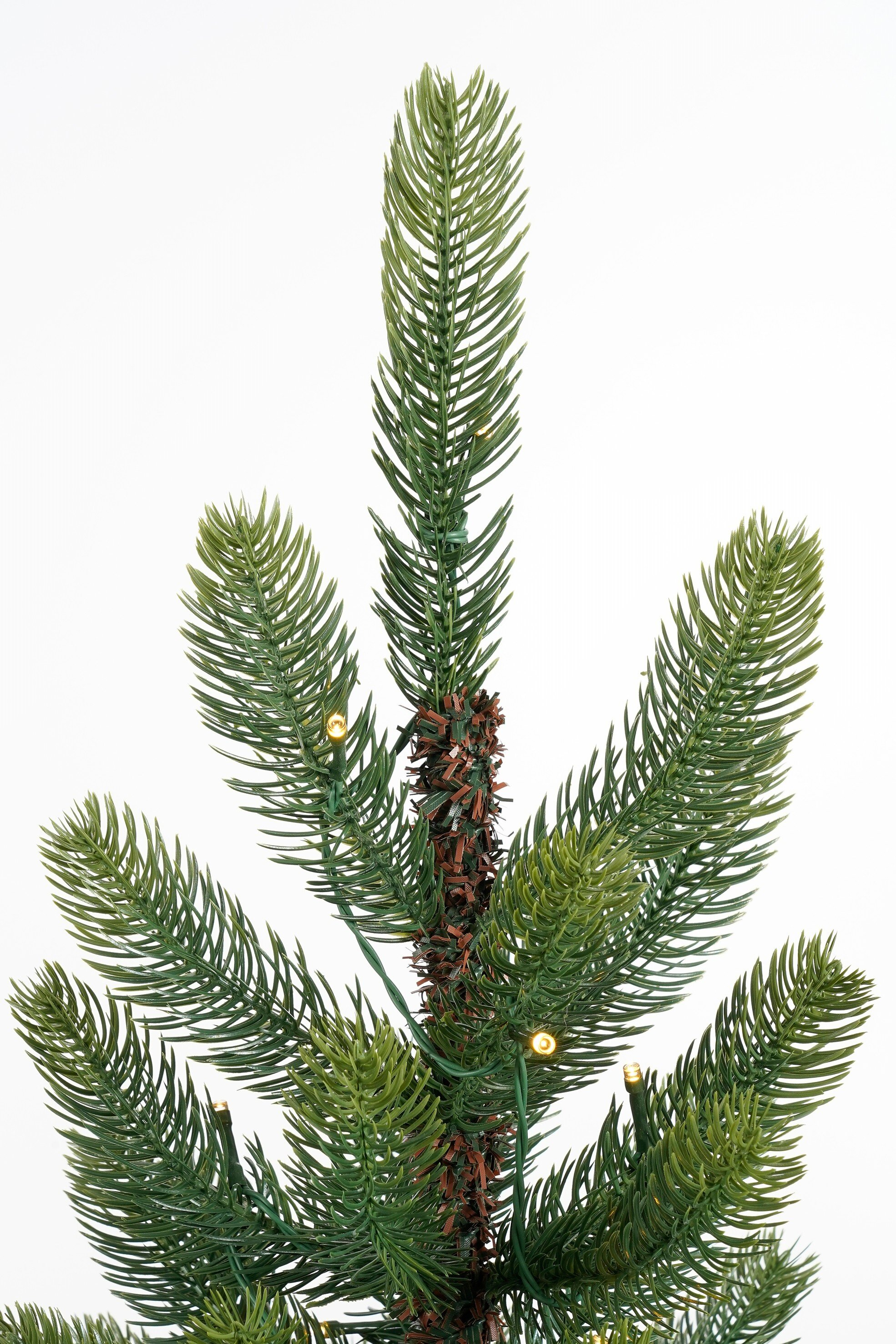 Close-up van een groene kunstkerstboom met kleine gele lampjes. De achtergrond is wit.