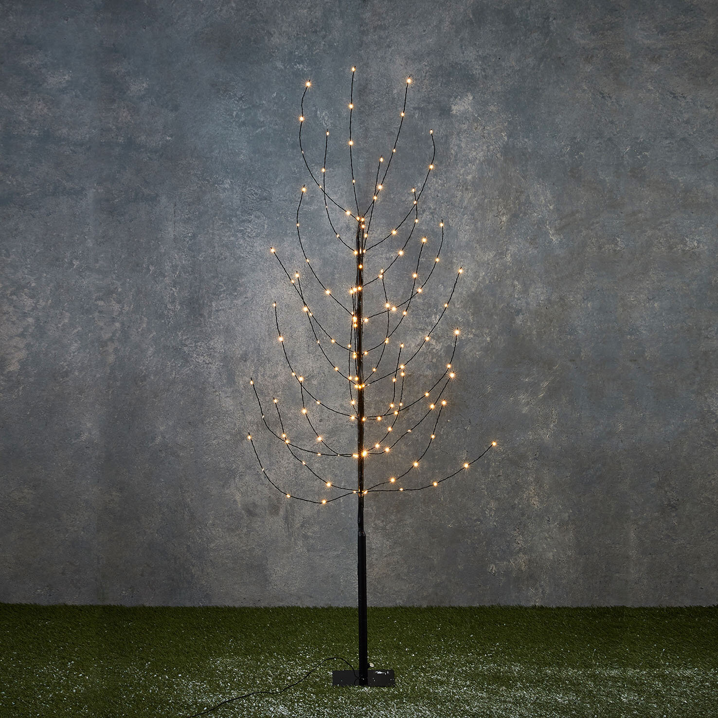 Un arbre décoratif avec de nombreuses petites lumières sur une surface verte, contre un mur gris.