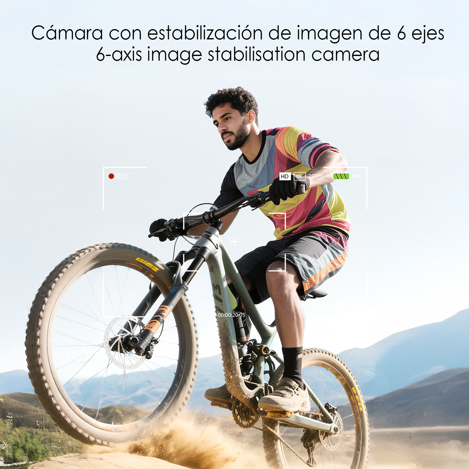 Mann fährt Mountainbike. Das Fahrrad wirbelt Sand auf. Der Mann trägt ein buntes Hemd und schwarze Shorts. Im Hintergrund ist ein Berg.