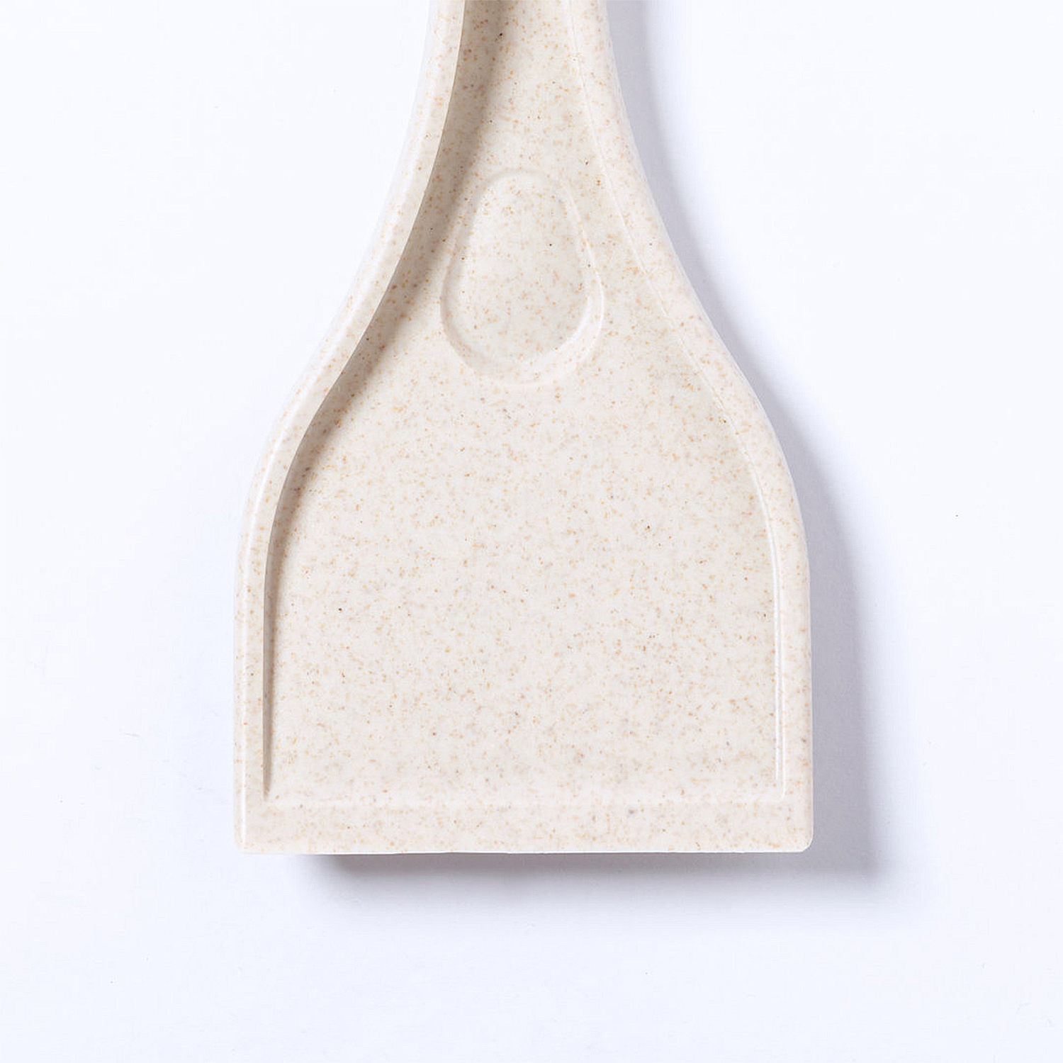 Una espátula beige con una cabeza ancha y rectangular y un mango. La superficie tiene pequeñas motas oscuras. Está sobre un fondo blanco.