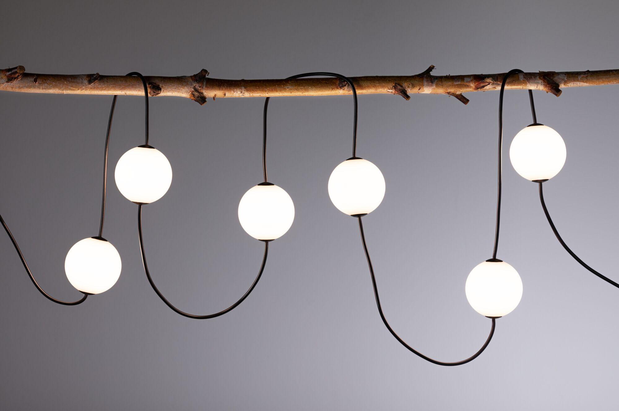 Drewniana gałąź z sześcioma świecącymi kulistymi światłami wiszącymi na niej na szarym tle. Przewody są czarne.
