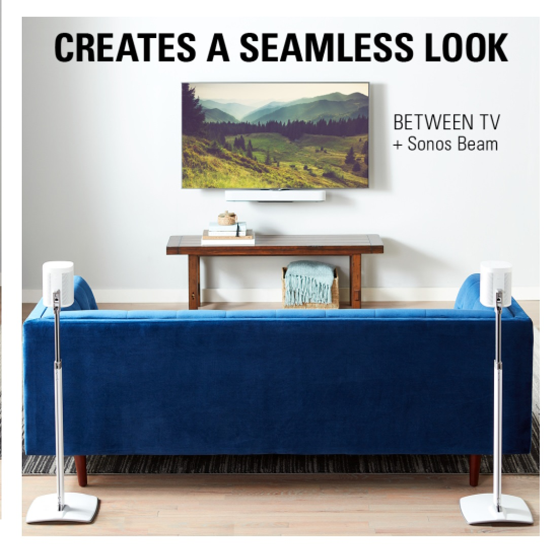 Living room setup with blue sofa, TV, wooden table, and speakers. TV shows landscape. Speakers are on stands.