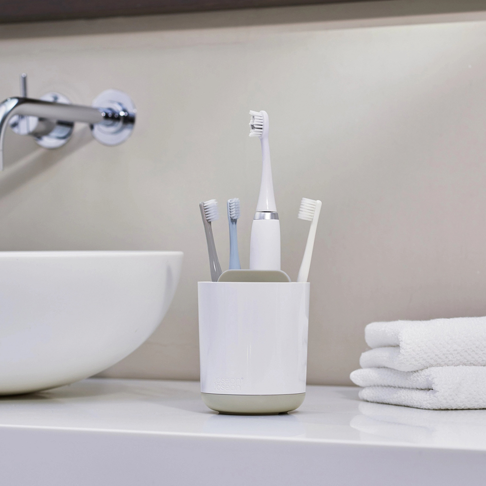 Escena de baño con cepillos de dientes en un soporte, toallas y un lavabo. Los cepillos tienen colores. El fondo está borroso.