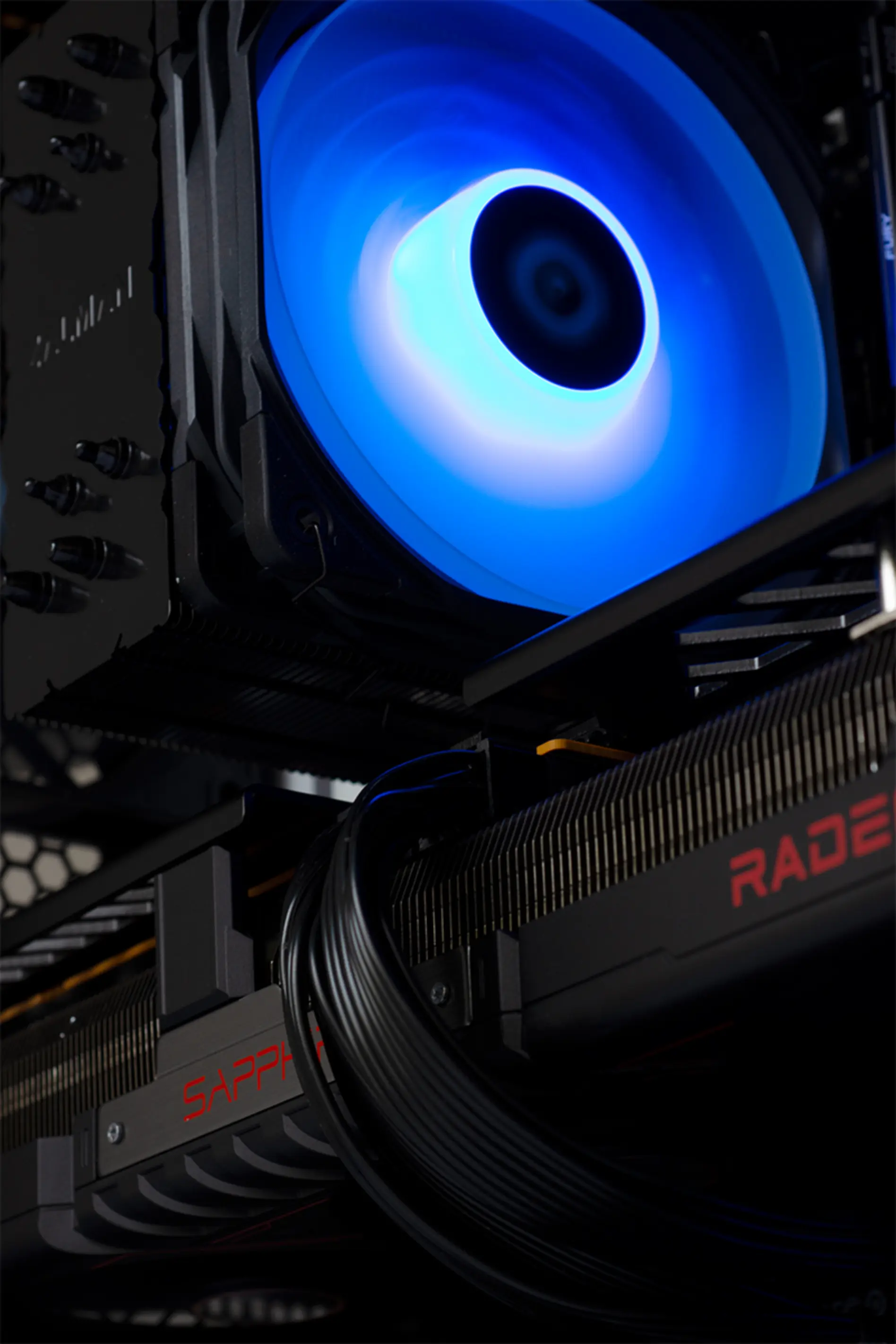PC-componenten: een blauw verlichte CPU-koeler, grafische kaart met 'RADEON' tekst en zwarte kabels.