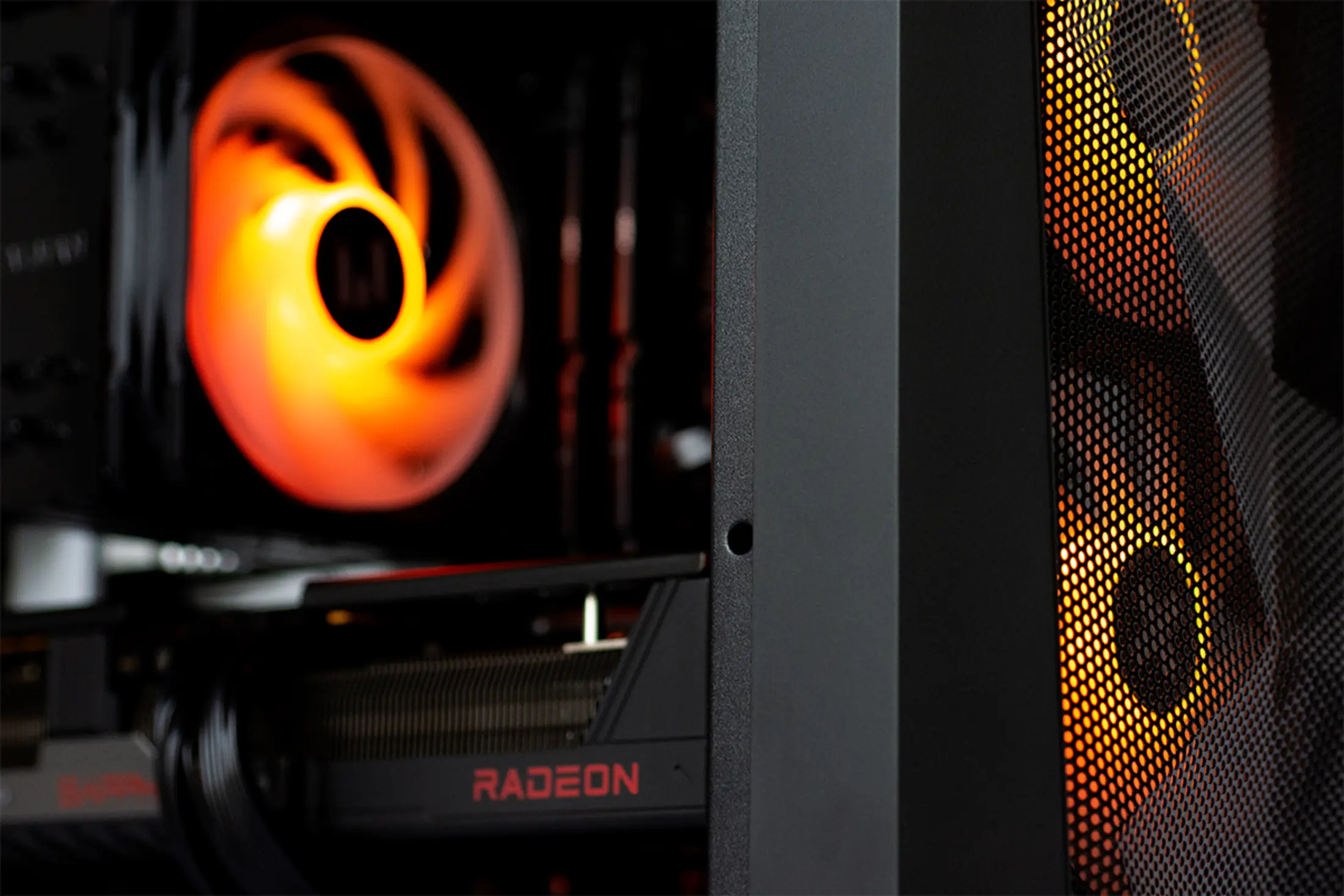 PC-interieur. Oranje gloeiende ventilator, zwarte behuizing en Radeon grafische kaart zijn zichtbaar. De behuizing heeft een gaas.