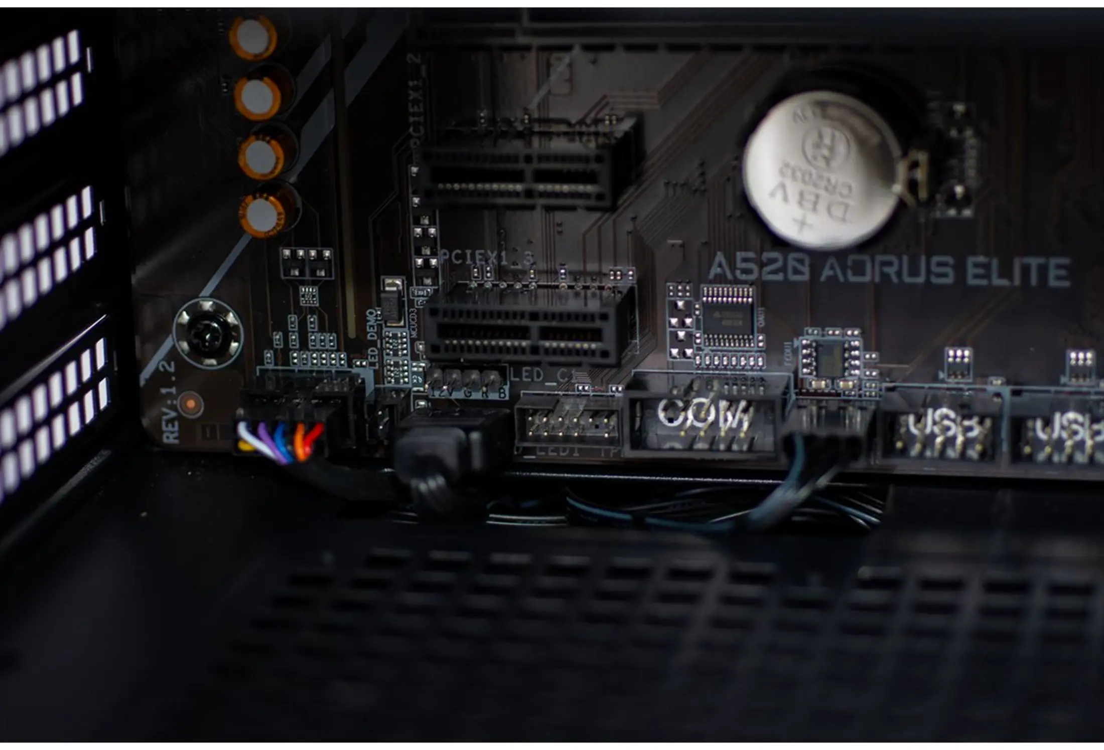 Close-up van een computer moederbord. Zichtbare componenten zijn slots, een batterij en diverse connectoren met gekleurde draden.