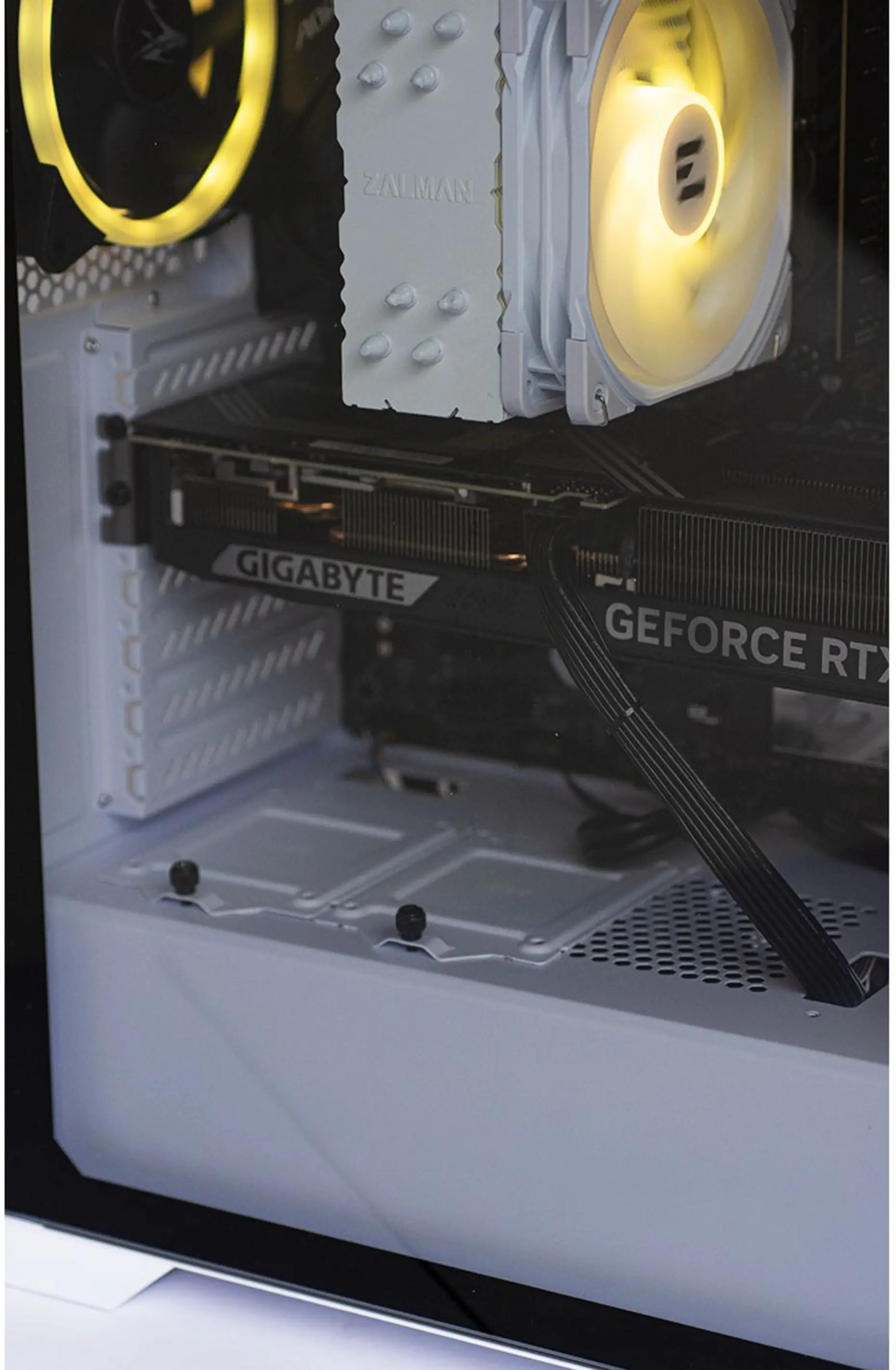 PC-componenten in een witte behuizing, waaronder een grafische kaart van Gigabyte en een Zalman-koeler. Ventilatoren gloeien geel.