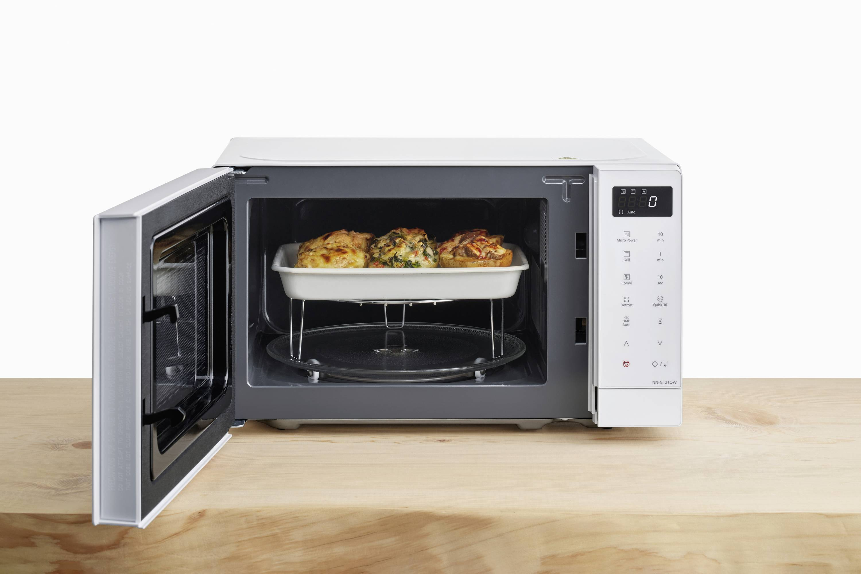 Un forno a microonde bianco con la porta aperta. All'interno, un vassoio contiene tre piatti cotti.