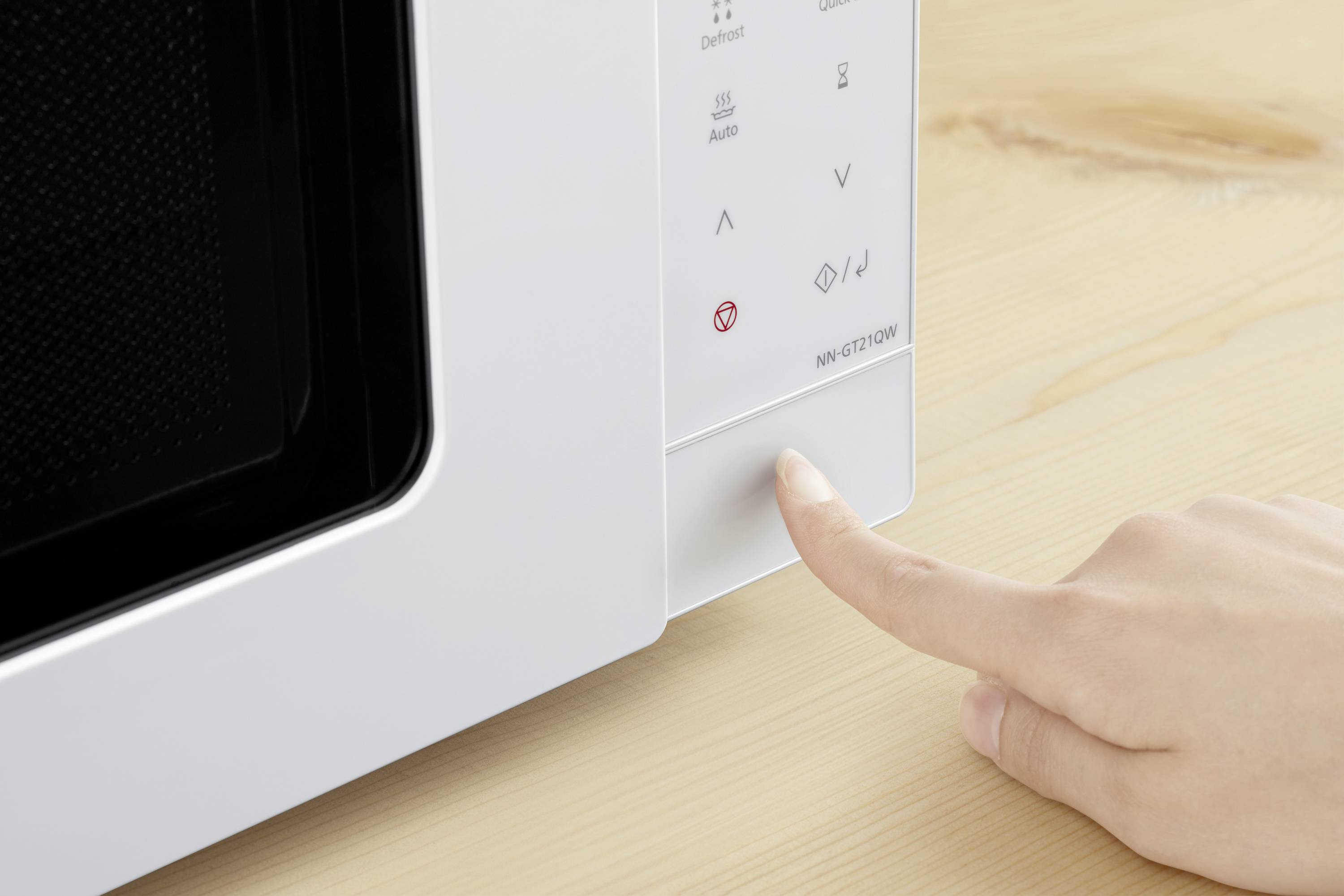 Una mano preme un pulsante su un forno a microonde bianco. Il forno è su legno chiaro.