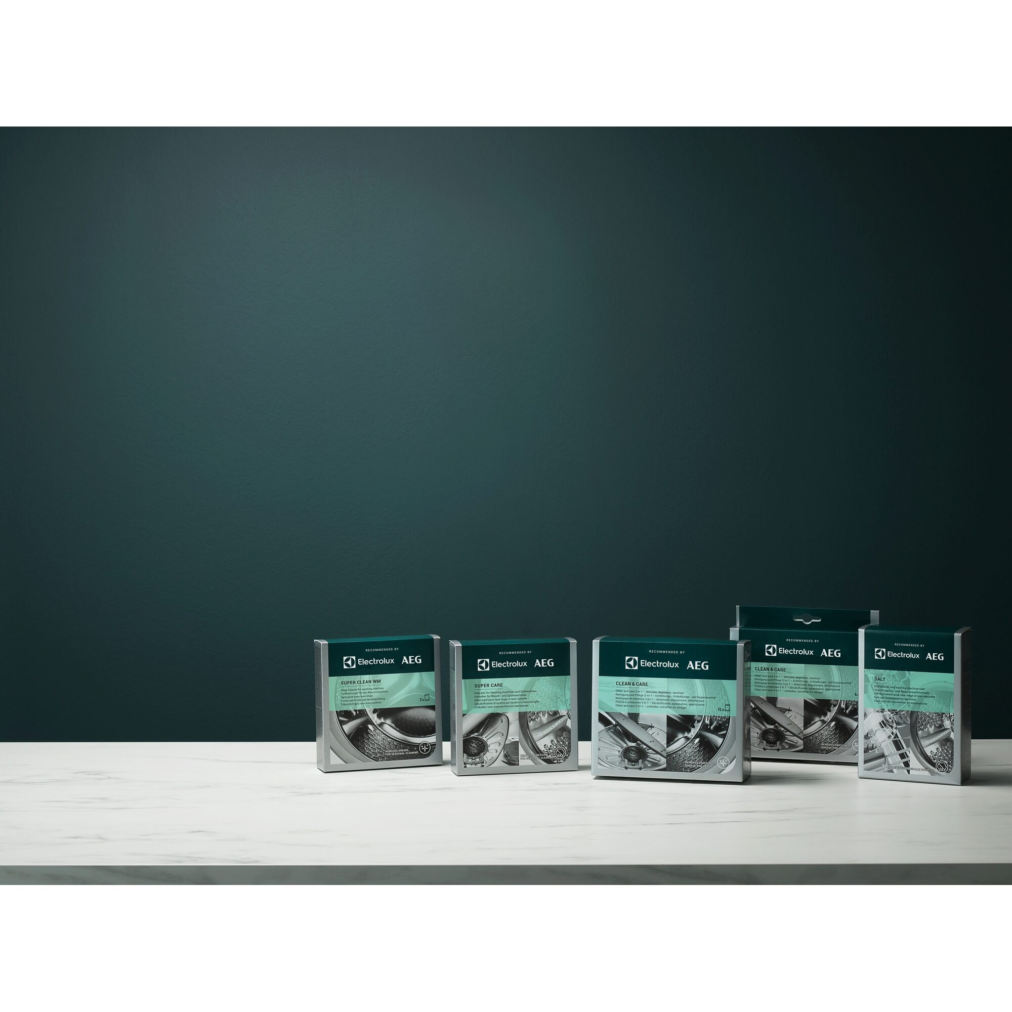 Plusieurs boîtes de produits de nettoyage Electrolux AEG sont sur une surface blanche. Le fond est de couleur vert-bleu foncé.