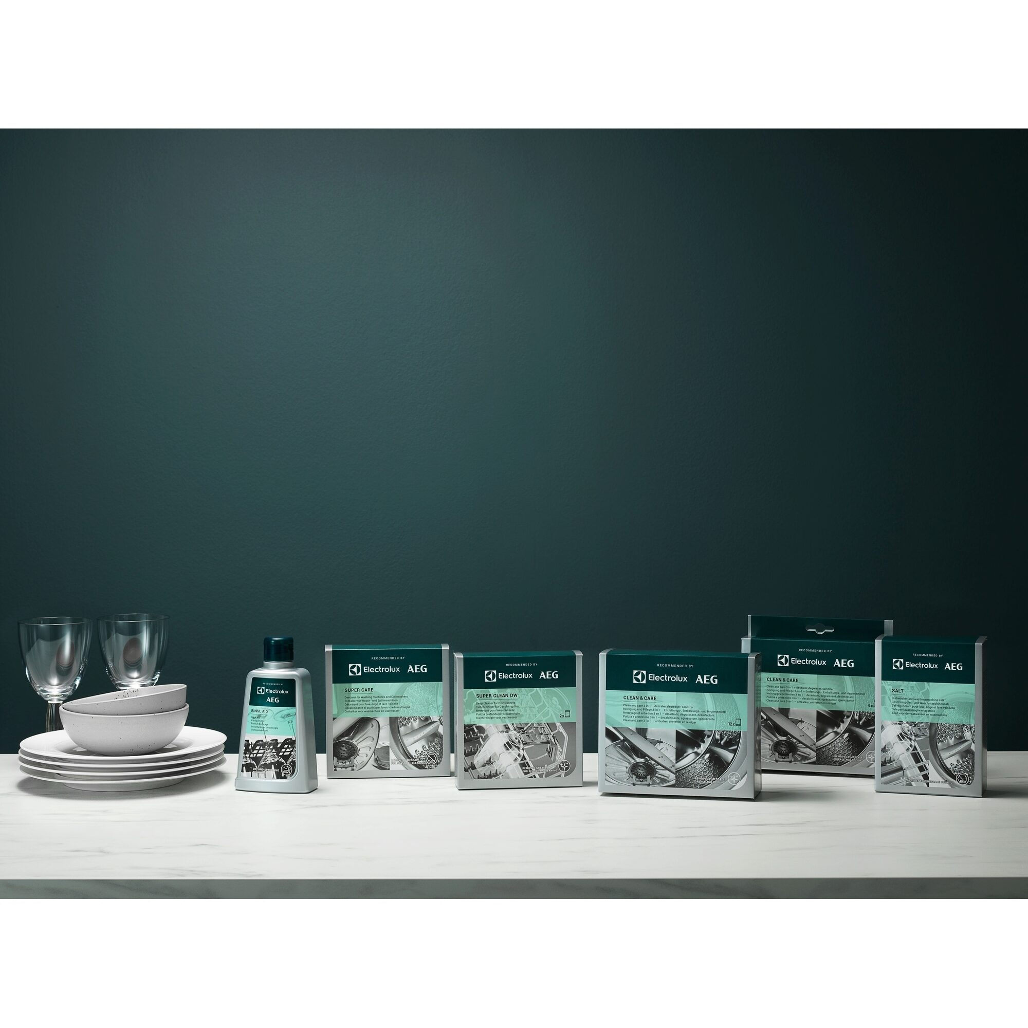 Photo de produits avec produits de nettoyage, assiettes, verres et fond vert foncé sur surface blanche.