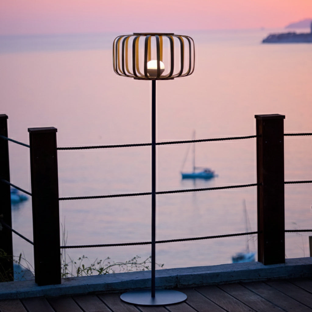 Eine moderne Außenlampe mit rundem Oberteil und heller Glühbirne. Im Hintergrund sind Meer, Himmel und Boote zu sehen.