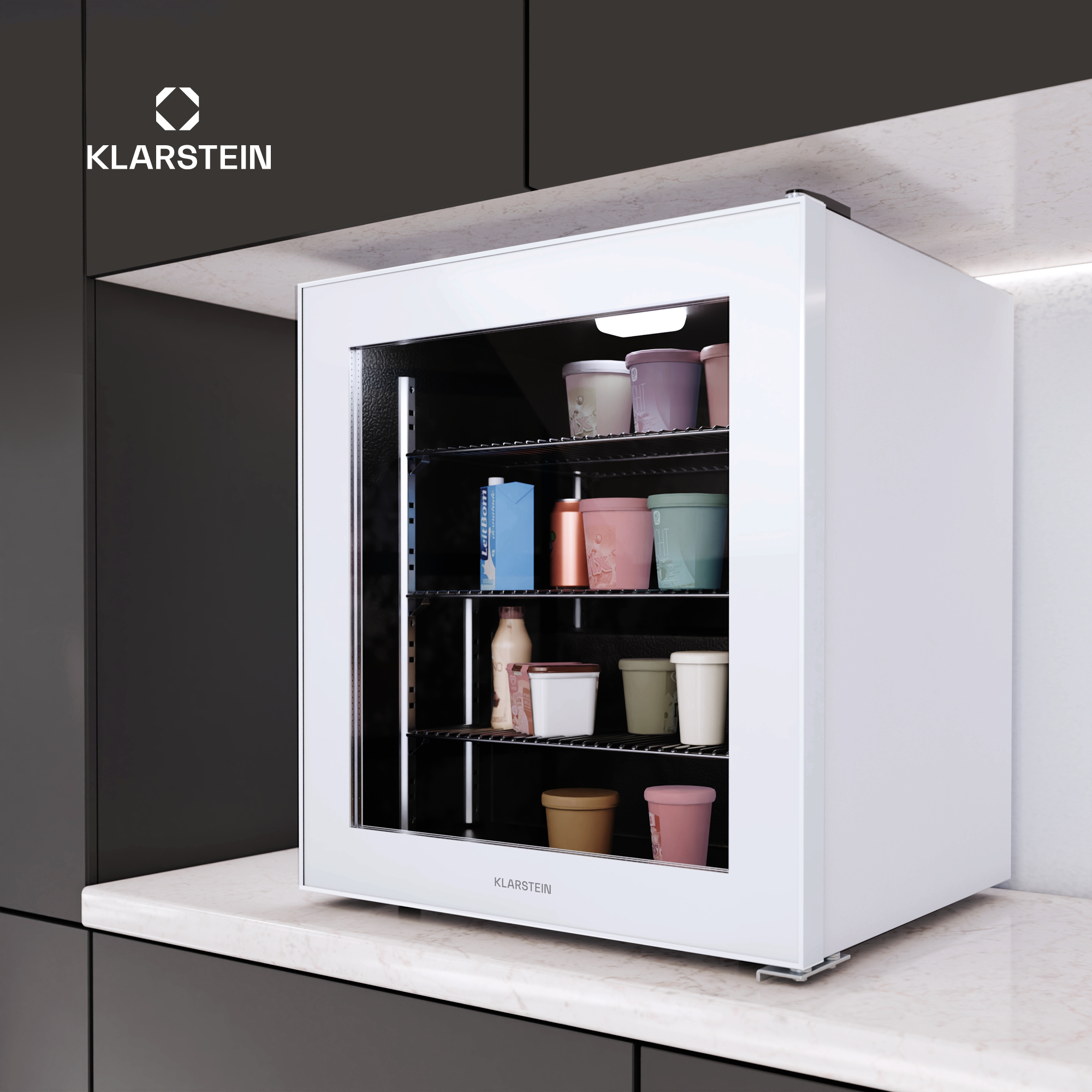 Un mini frigo Klarstein bianco con porta a vetro, pieno di vari contenitori di gelato, poggia su un piano di lavoro in marmo.
